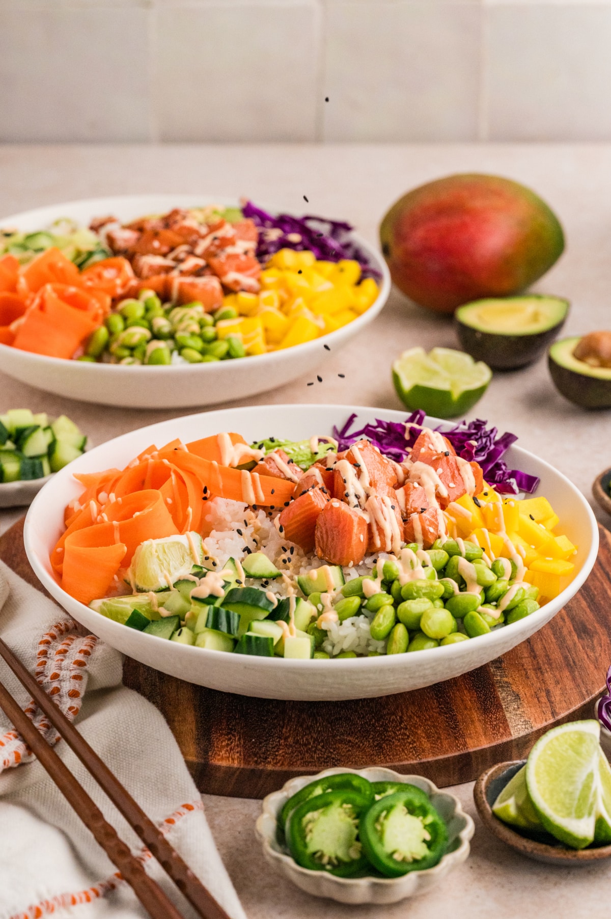 Wide serving shot of prepared poke bowls arranged with fresh fruit, vegetables, and cubed raw salmon, with lime wedges on the side Salmon poke bowl served with sushi rice, marinated salmon, mango, edamame, cucumber, and avocado