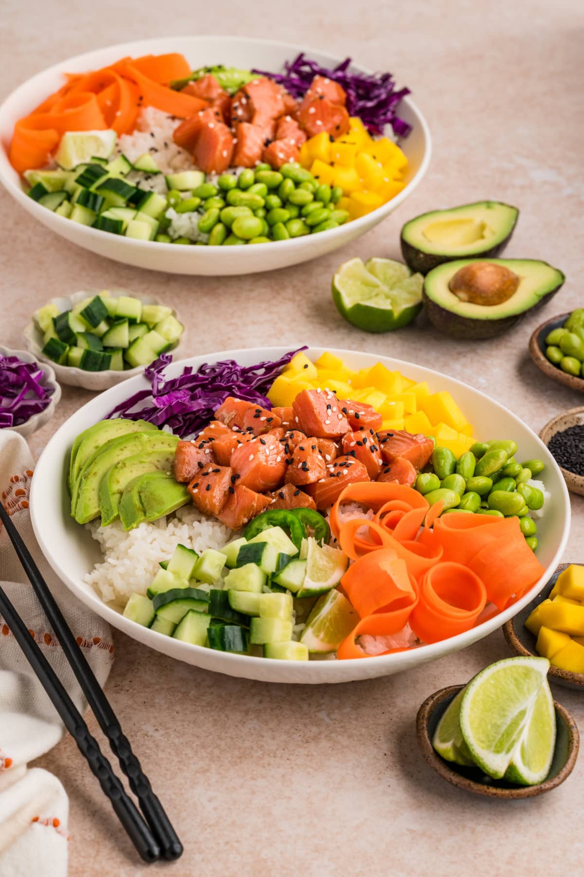 Angled view of a prepared poke bowl with raw salmon, rice, fresh vegetables, and fruit arranged in sections Two salmon poke bowls with sushi rice, mango, avocado, edamame, cucumber, and marinated salmon