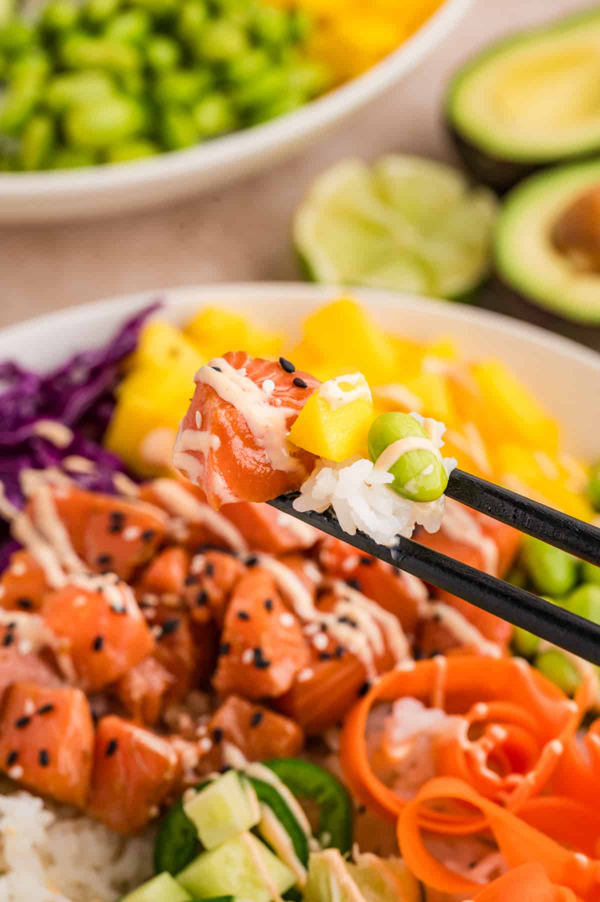 Close-up action shot of a bite of poke bowl ingredients lifted with chopsticks, showing salmon, rice, fruit, and vegetables Salmon poke bowls bite with marinated salmon, sushi rice, mango, and edamame held with chopsticks