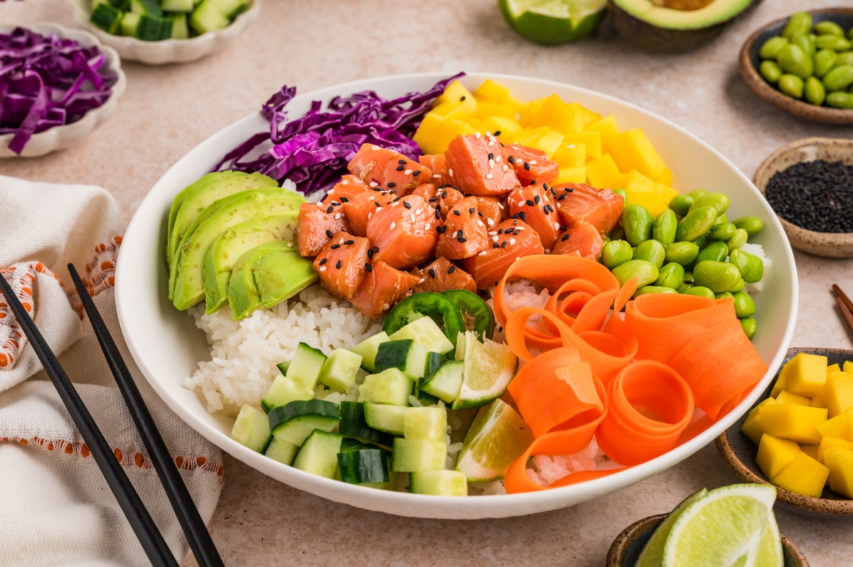 Wide overhead view of a poke bowl filled with marinated salmon, rice, fresh fruit, and colorful vegetables arranged in sections Salmon poke bowl with sushi rice, mango, avocado, edamame, cucumber, and shredded carrots
