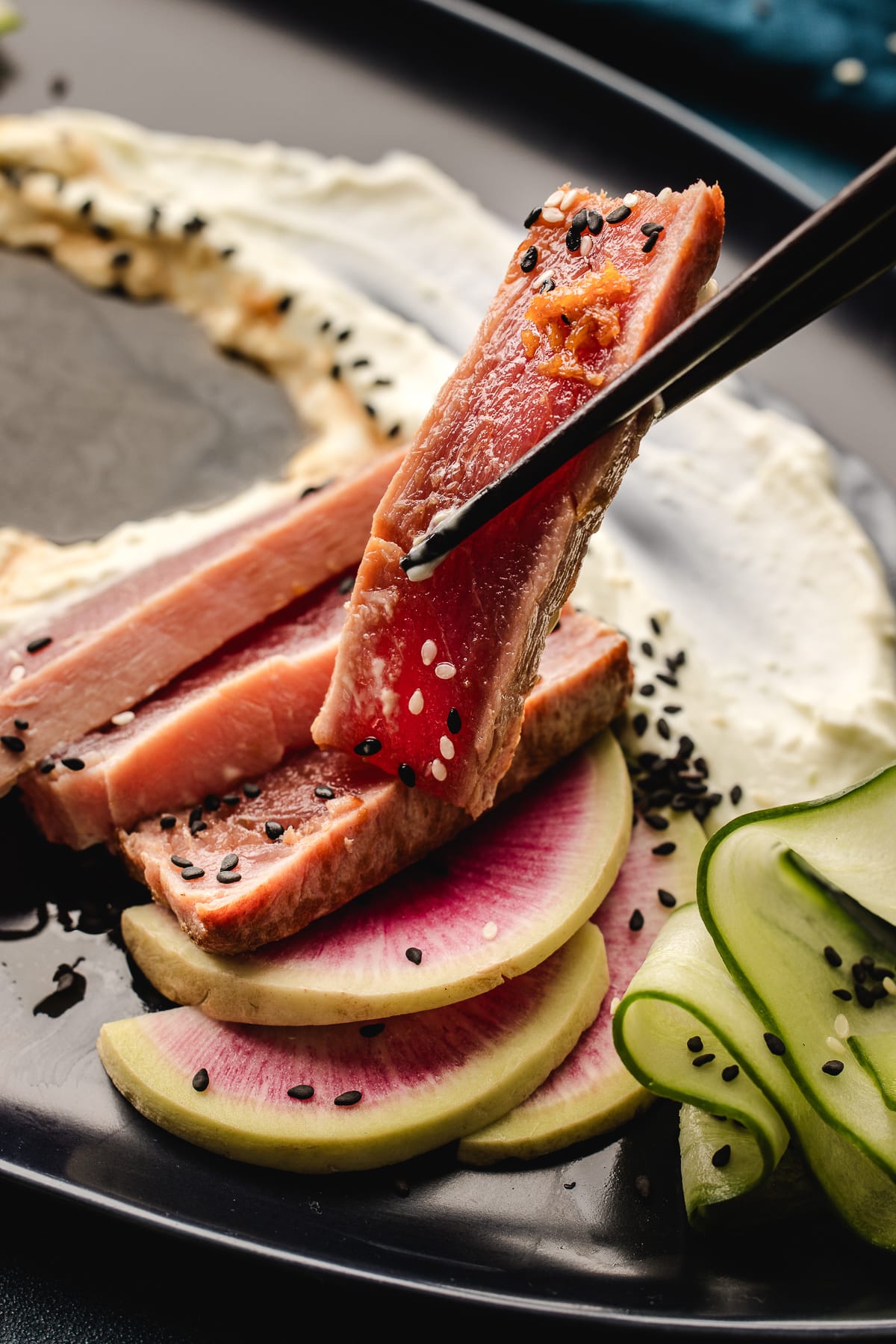 Seared ahi tuna lifted with chopsticks showing rare pink center and sesame seeds
