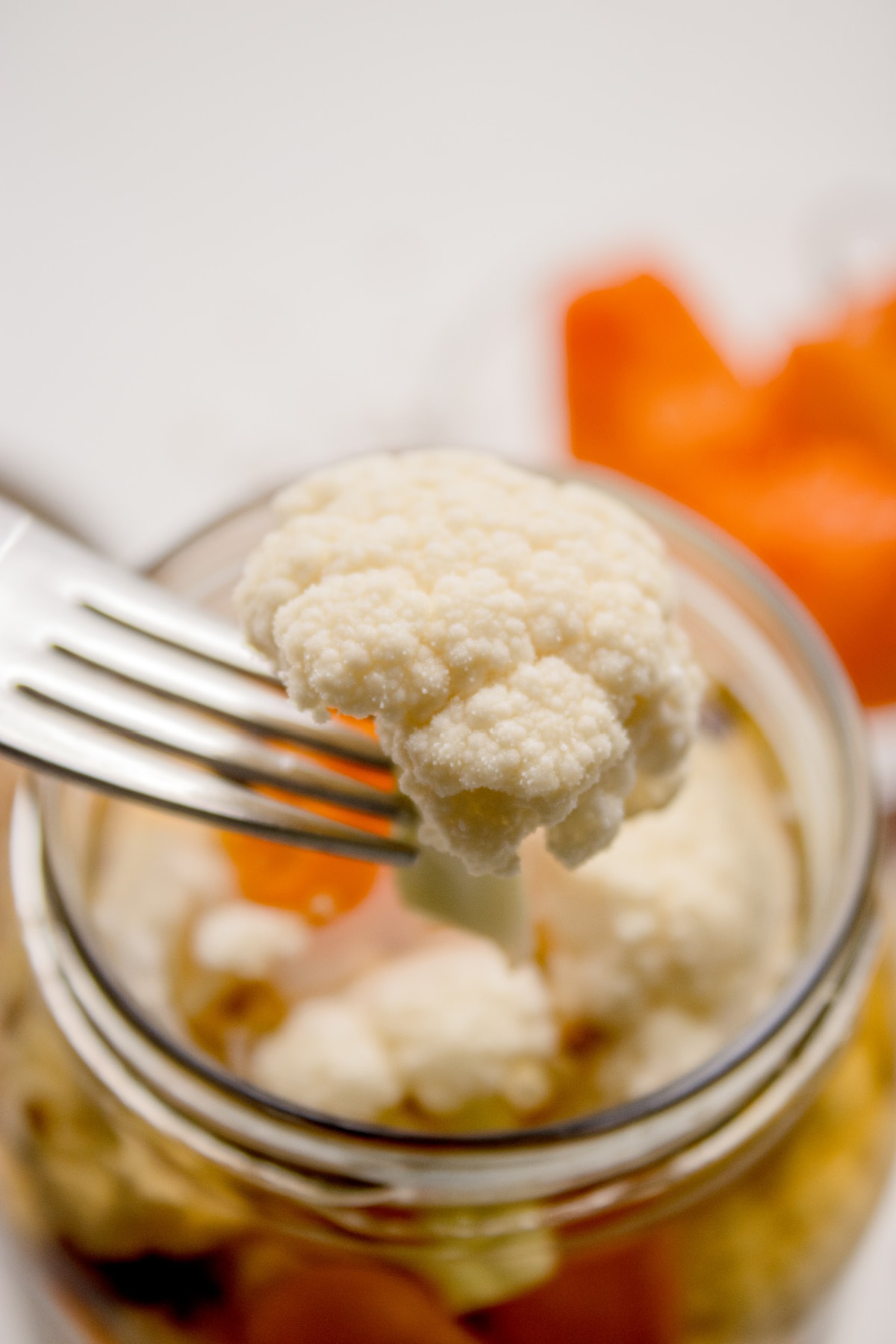 Close-up of crunchy refrigerator pickled cauliflower bite Fork lifting a crisp cauliflower floret from spicy vinegar brine in glass jar