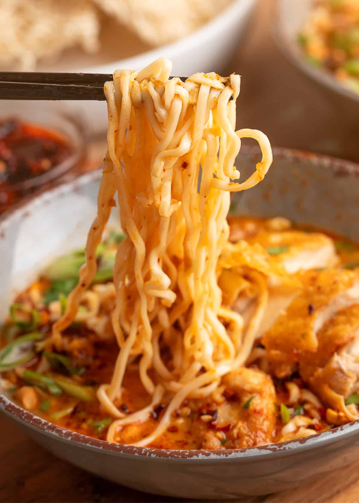 Thai coconut curry ramen noodles lift Chopsticks lifting ramen noodles from Thai coconut curry ramen with crispy chicken, chili oil, and scallions