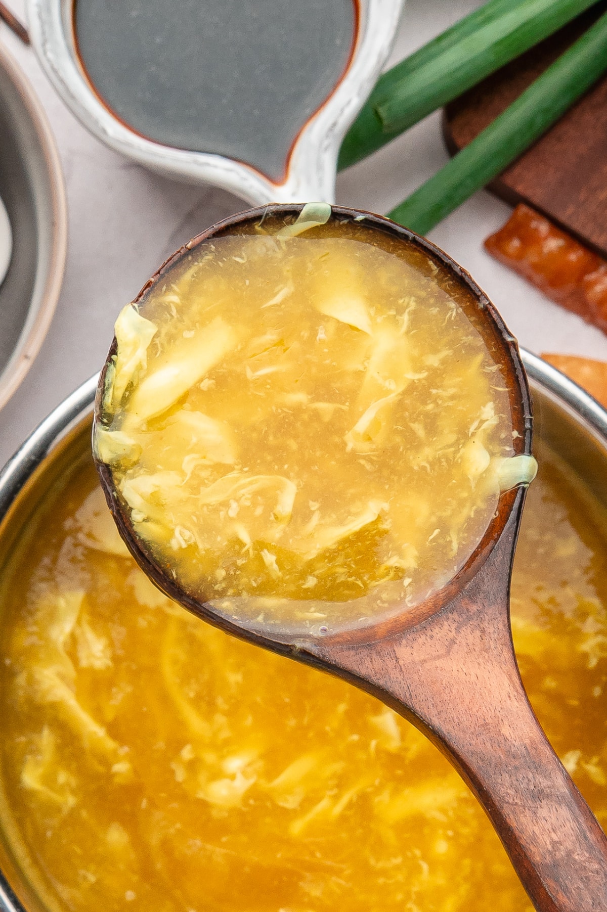 Close-up of a ladle lifting egg drop soup with delicate egg ribbons suspended in a lightly thickened golden broth Close-up of egg drop soup showing soft egg ribbons in broth