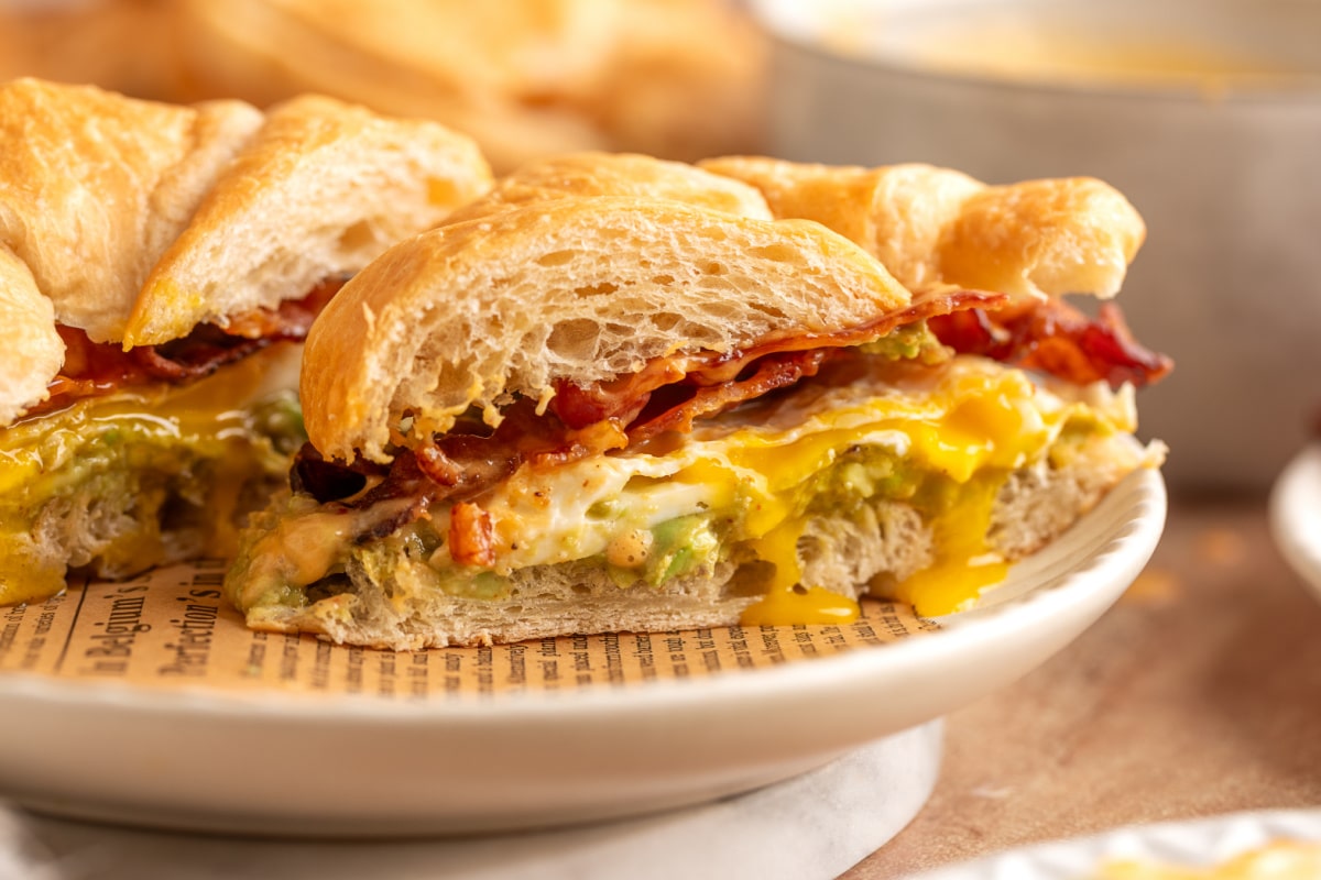 Bacon egg avocado breakfast sandwich cut in half with runny yolk, crispy bacon and chipotle hollandaise on a flaky croissant
