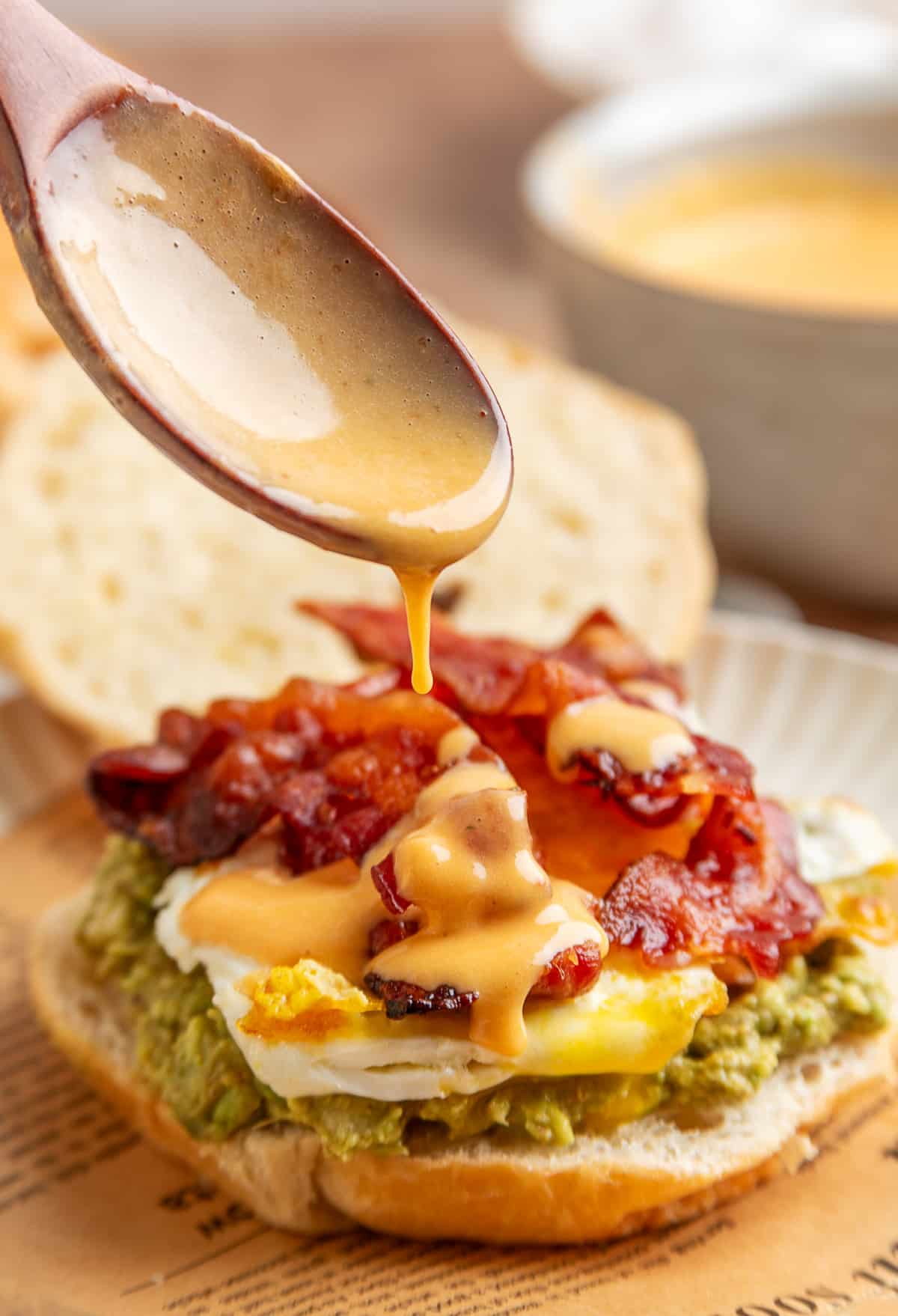 Bacon egg avocado breakfast sandwich on a croissant with crispy bacon, sunny side egg, mashed avocado and lime chipotle hollandaise dripping on top