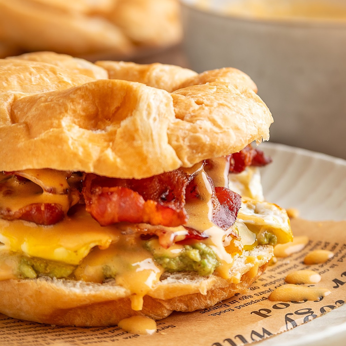 Bacon egg avocado breakfast sandwich on a flaky croissant with crispy bacon and chipotle hollandaise