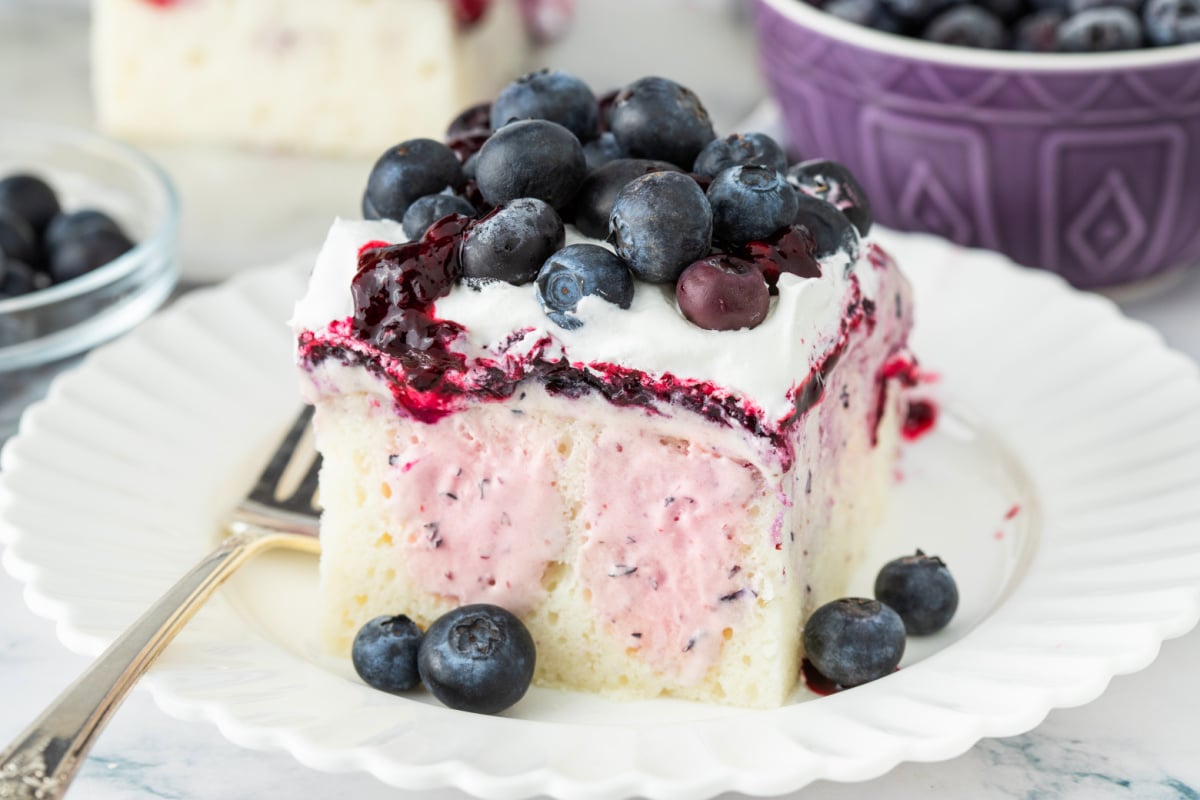 Blueberry cheesecake poke cake slice Slice of blueberry cheesecake poke cake showing creamy filling and blueberry layers