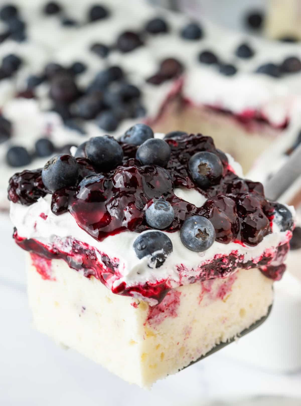 Blueberry cheesecake poke cake slice Slice of blueberry cheesecake poke cake with blueberry compote and whipped topping