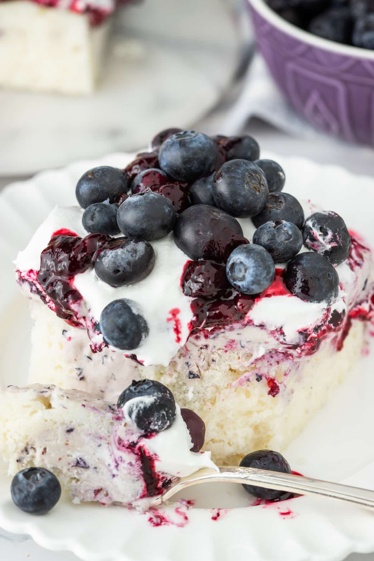 Blueberry poke cake slice Slice of blueberry poke cake with creamy filling, blueberry topping, and fresh berries