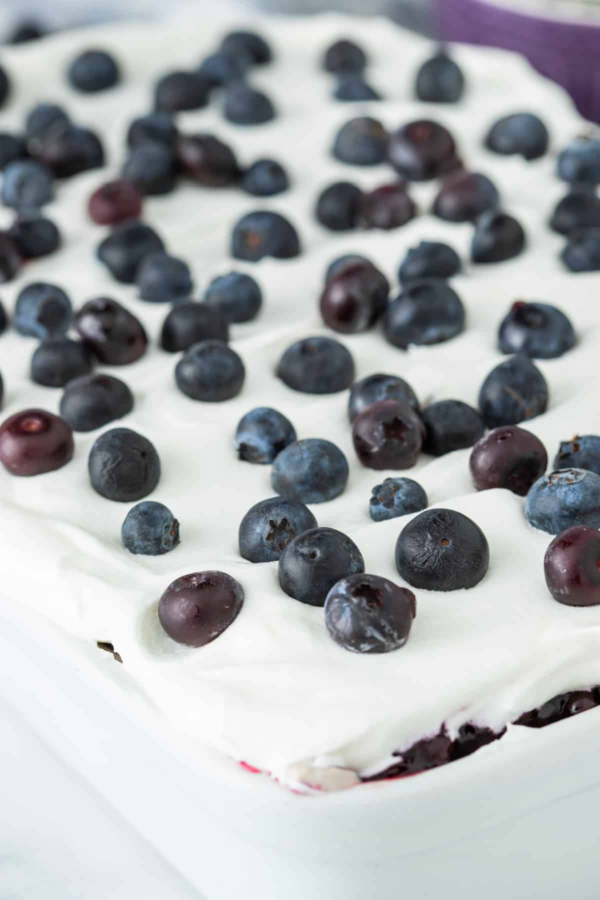 Blueberry poke cake with whipped topping Blueberry poke cake topped with whipped topping and fresh blueberries in a baking dish