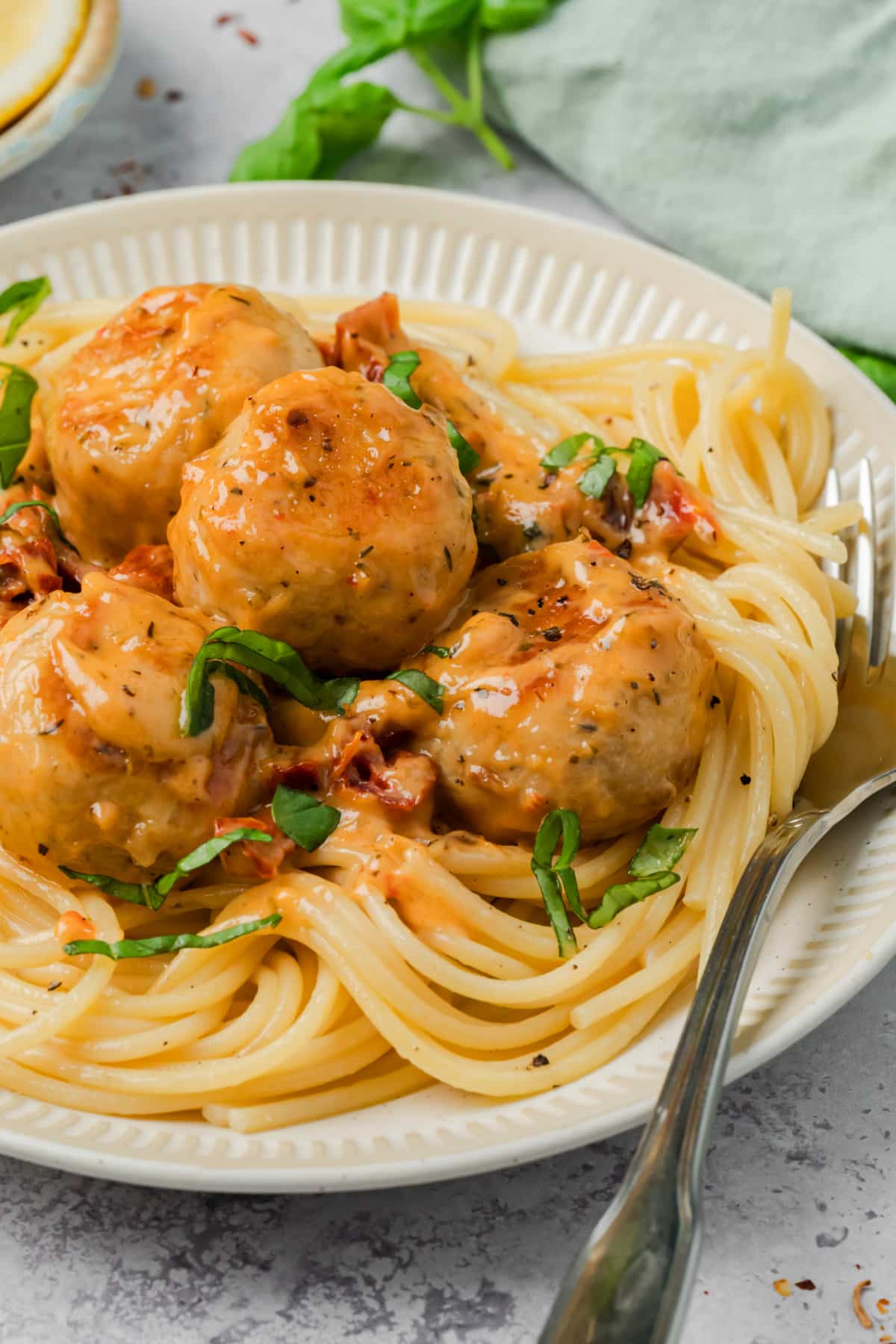 Creamy chicken meatballs with sun-dried tomato sauce served over spaghetti and topped with fresh basil