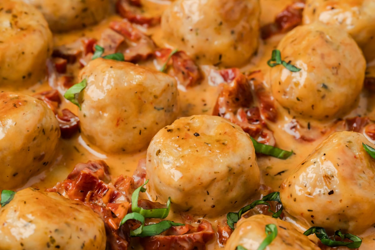 Close-up of creamy chicken meatballs simmered in sun-dried tomato Parmesan sauce with fresh basil