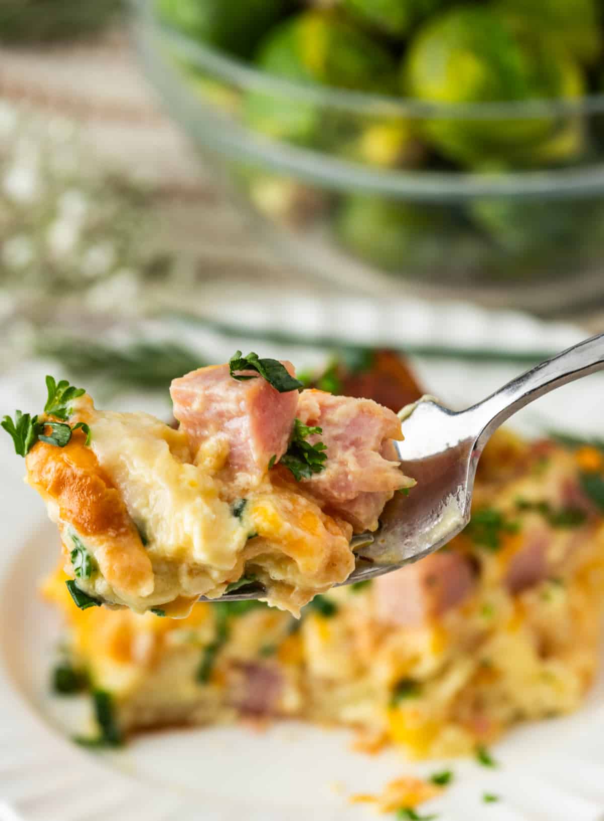 Croissant Breakfast Bake Bite with Ham and Cheese forkful of croissant breakfast bake with ham, melted cheese, egg custard, and fresh herbs
