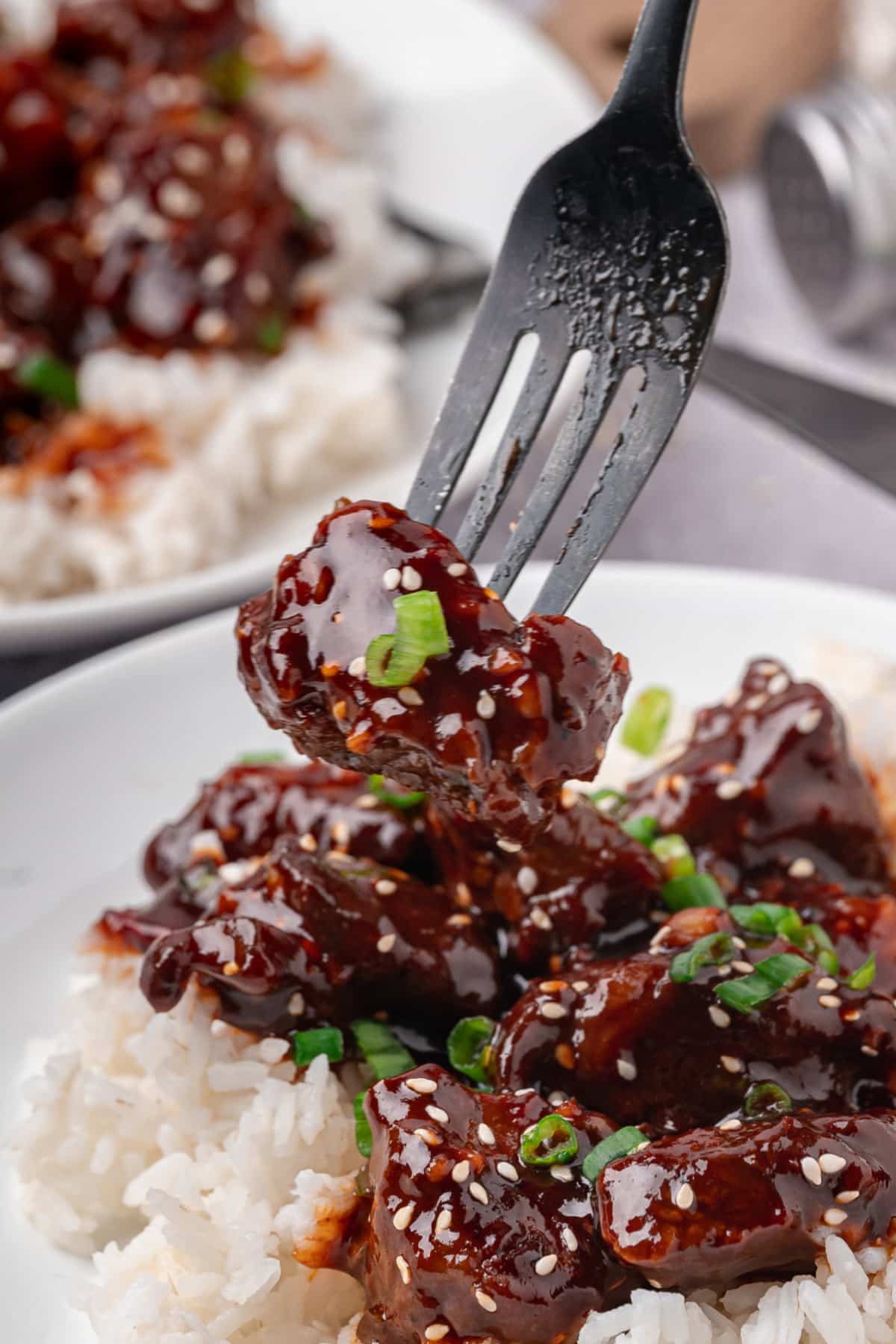 fork lifting gochujang steak bite over white rice with sesame seeds and green onions