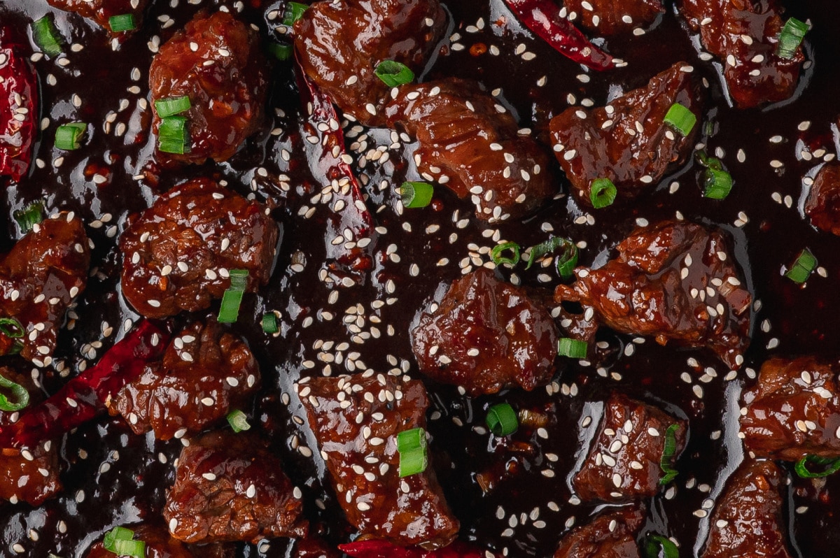 close up of gochujang steak bites in skillet with sesame seeds and green onions