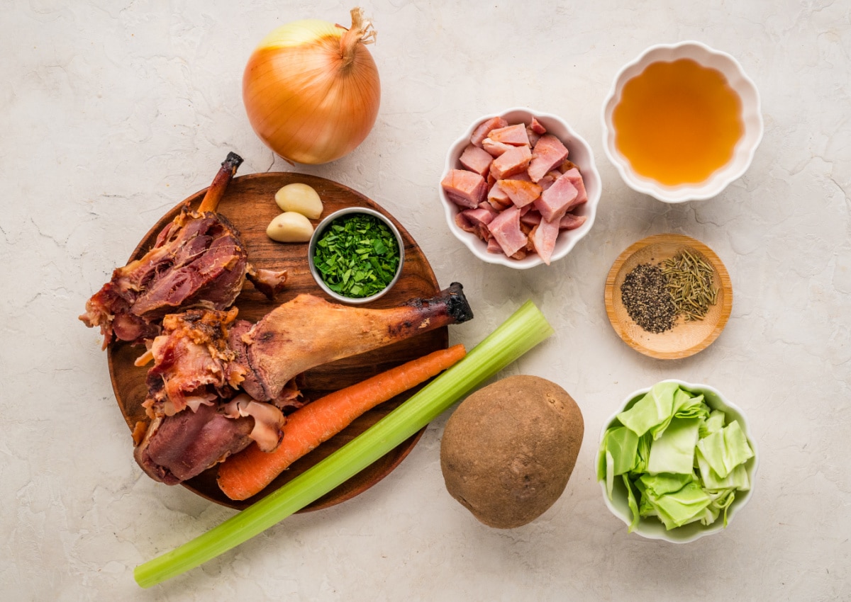 ham-and-cabbage-soup-ingredients Ingredients for ham and cabbage soup including ham hock, cabbage, potatoes, carrots, celery, onion, garlic, and broth