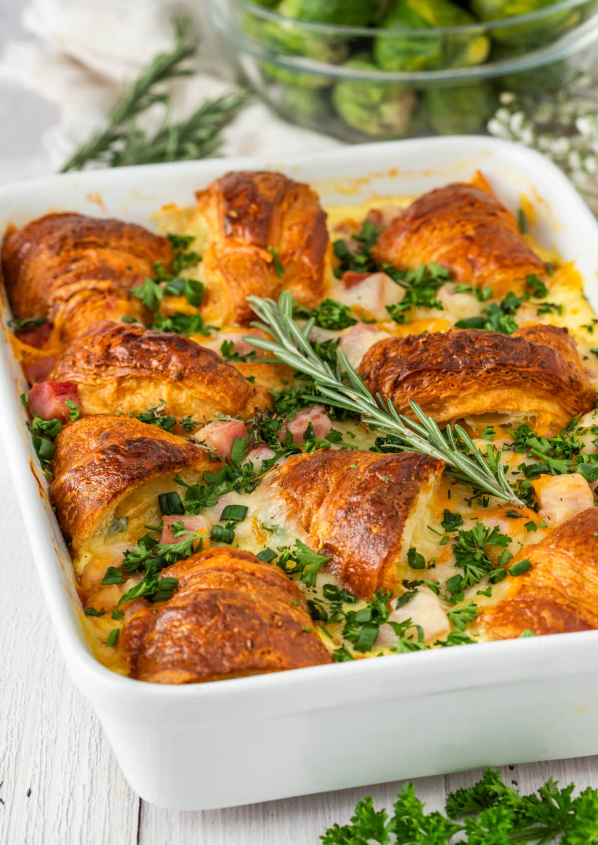 Ham and Cheese Croissant Breakfast Bake Casserole ham and cheese croissant breakfast bake with golden croissants, diced ham, melted cheese, and fresh herbs baked in a white casserole dish