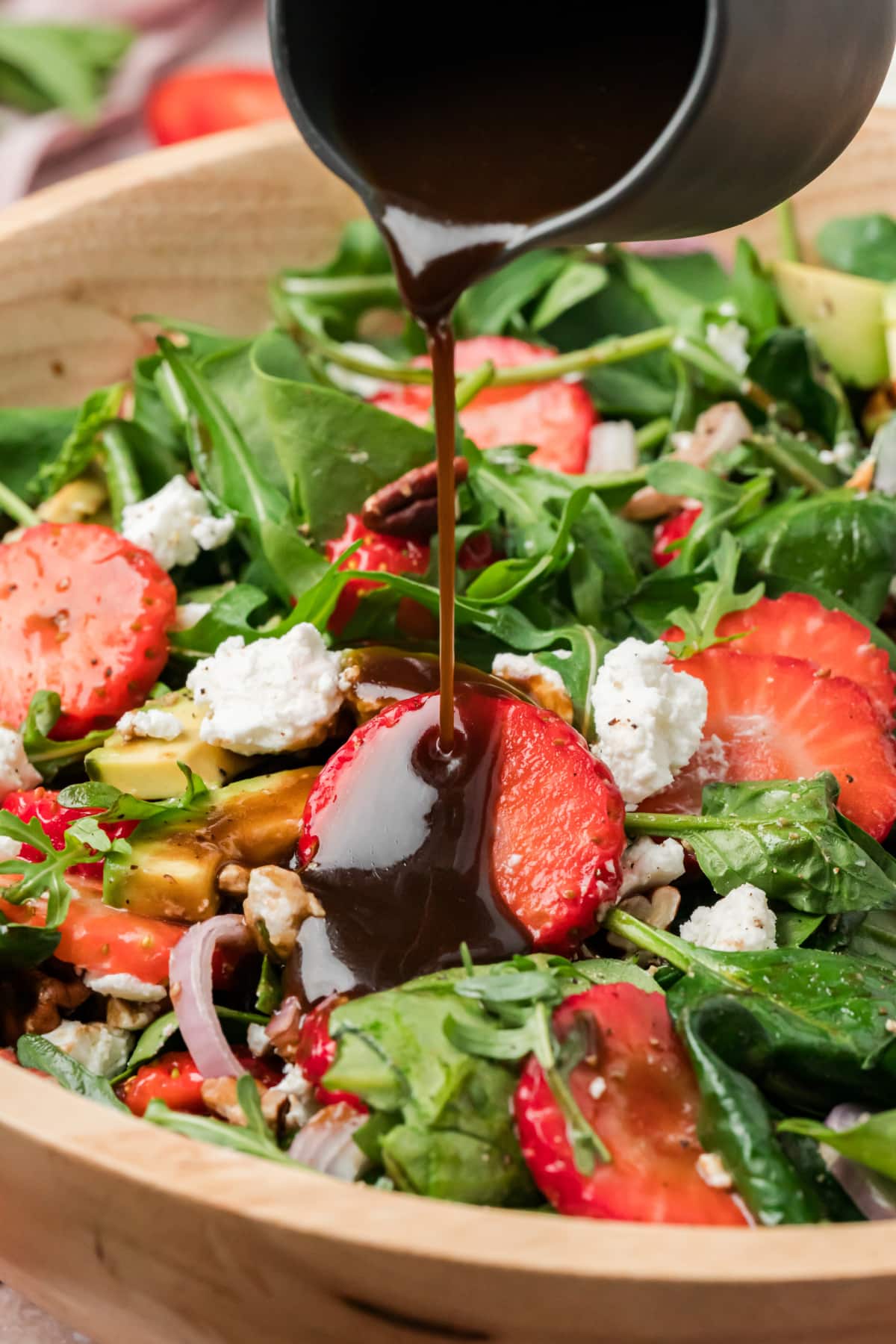 Strawberry Goat Cheese Salad with Balsamic Vinaigrette Being Poured Strawberry goat cheese salad with avocado, pecans, and greens as balsamic vinaigrette is poured over the top
