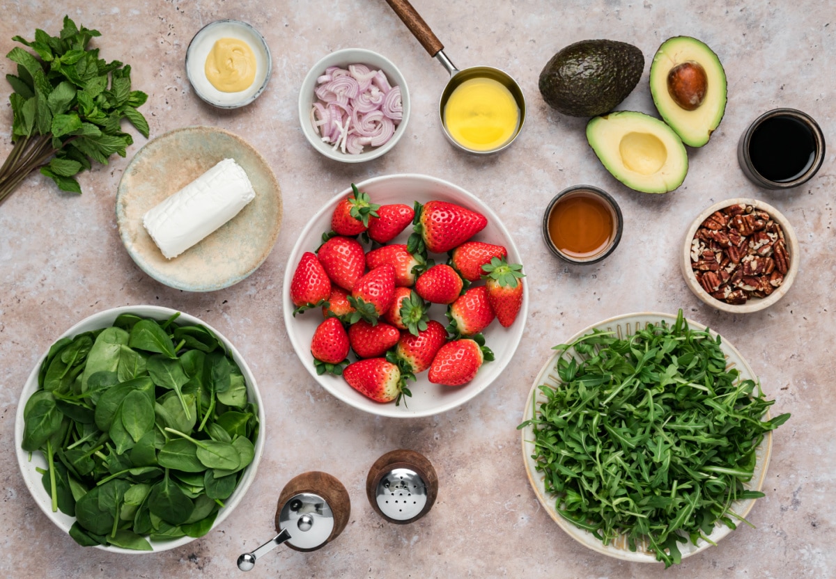 Ingredients for Strawberry Goat Cheese Salad with Spinach and Arugula Ingredients for strawberry salad with goat cheese including fresh strawberries, spinach, arugula, avocado, pecans, and balsamic vinaigrette