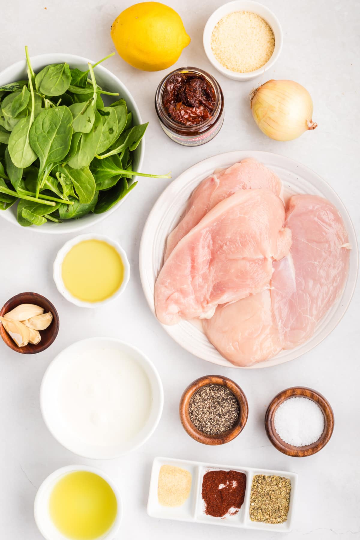 tuscan chicken ingredients with spinach and sun-dried tomatoes ingredients for tuscan chicken including chicken breasts, spinach, sun-dried tomatoes, garlic, lemon, and parmesan