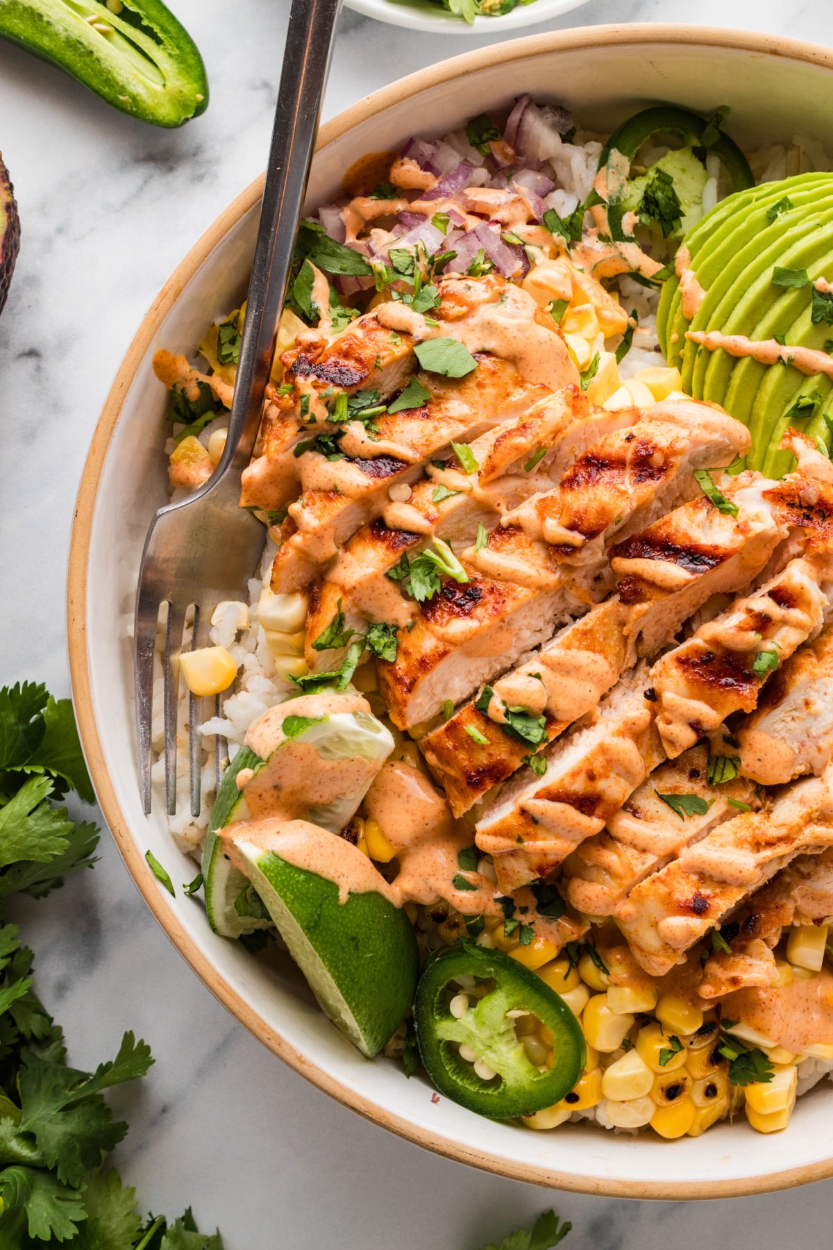 grilled chicken rice bowl with charred corn, avocado, lime wedge, jalapeños, and creamy elote-style sauce