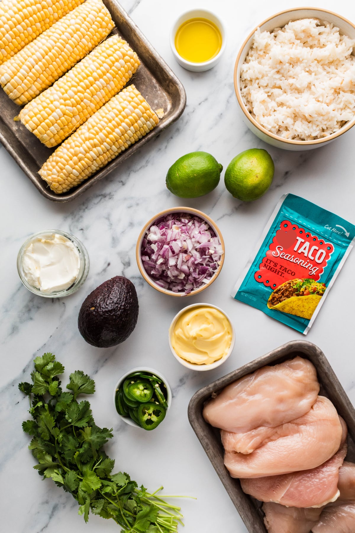 ingredients for chicken rice bowls including corn, rice, chicken breasts, avocado, lime, red onion, jalapeños, mayonnaise, and taco seasoning