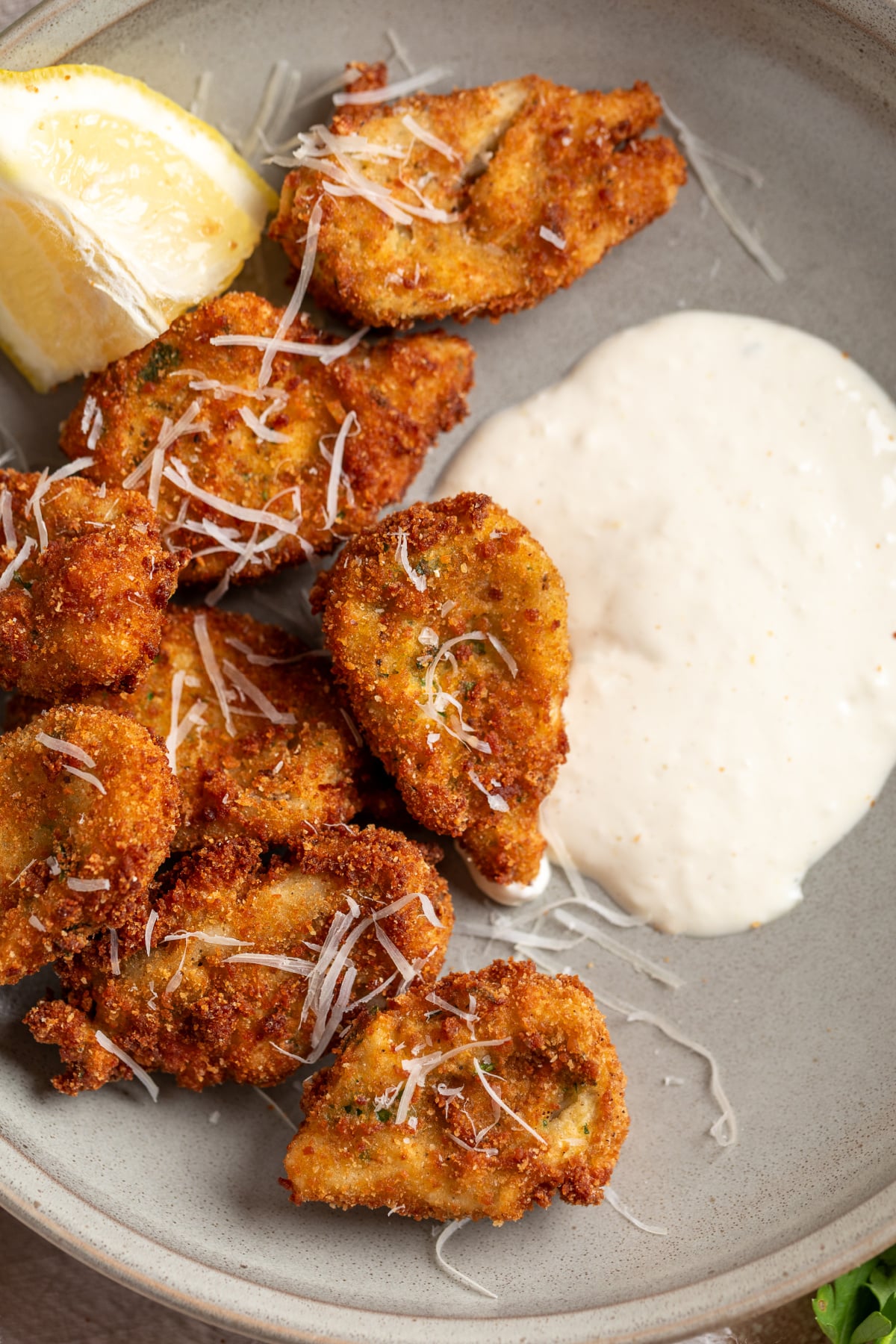 Crispy breaded artichoke hearts served with lemon garlic aioli and grated Parmesan on a plate
