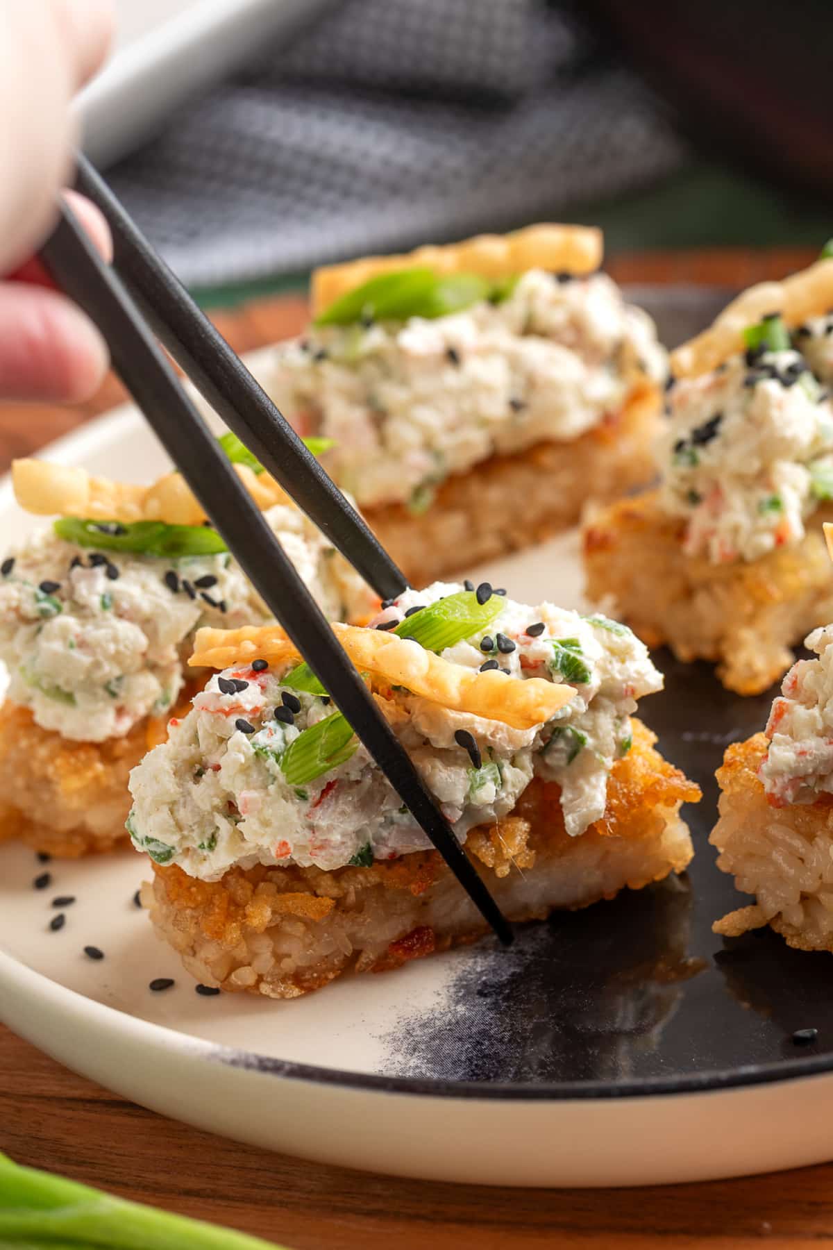 Crispy Rice Crab Rangoon Bites being picked up with chopsticks showing creamy crab topping and crispy rice base
