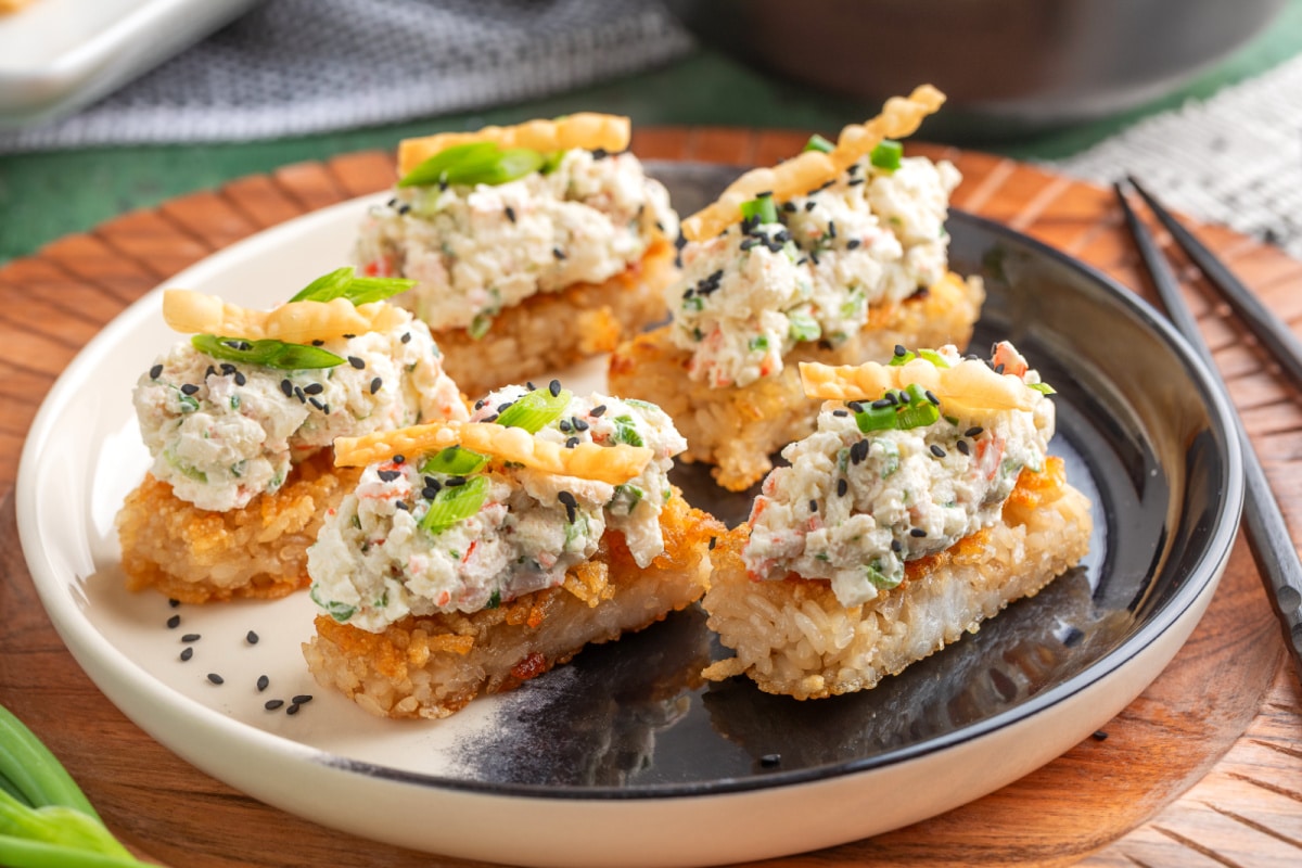 Crispy Rice Crab Rangoon Bites served on a plate with creamy crab topping, green onions, sesame seeds, and wonton strips