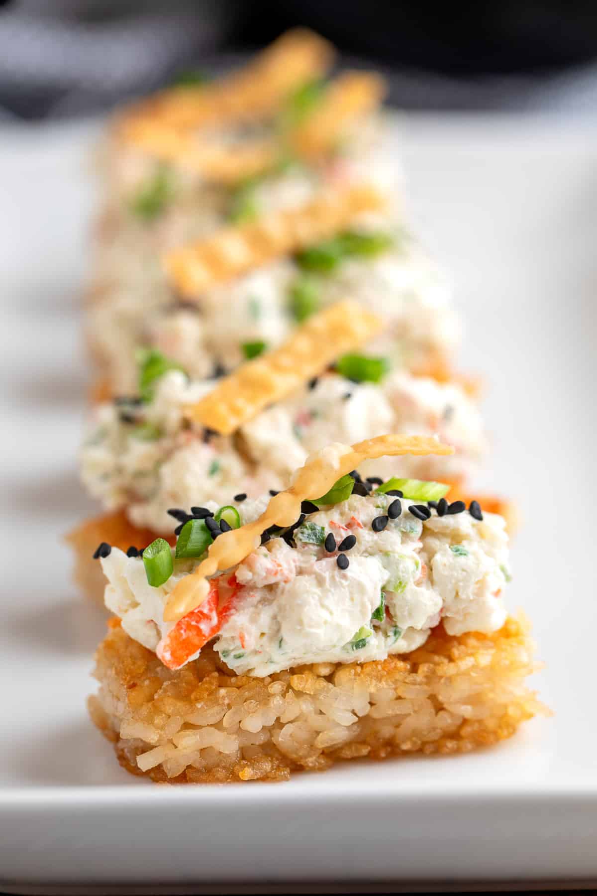 Crispy Rice Crab Rangoon Bites with creamy crab topping, green onions, sesame seeds, and wonton strips