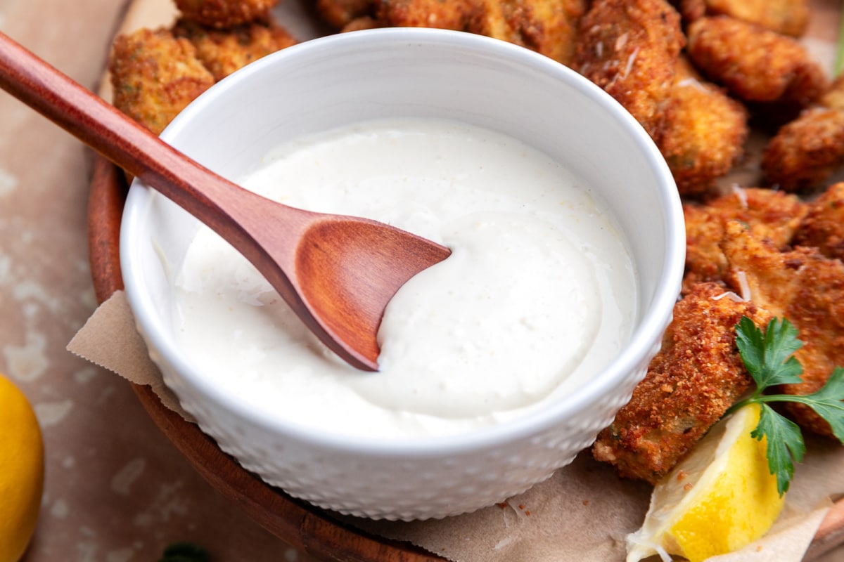 Fried artichokes with lemon garlic aioli in a white bowl with a spoon and lemon wedge
