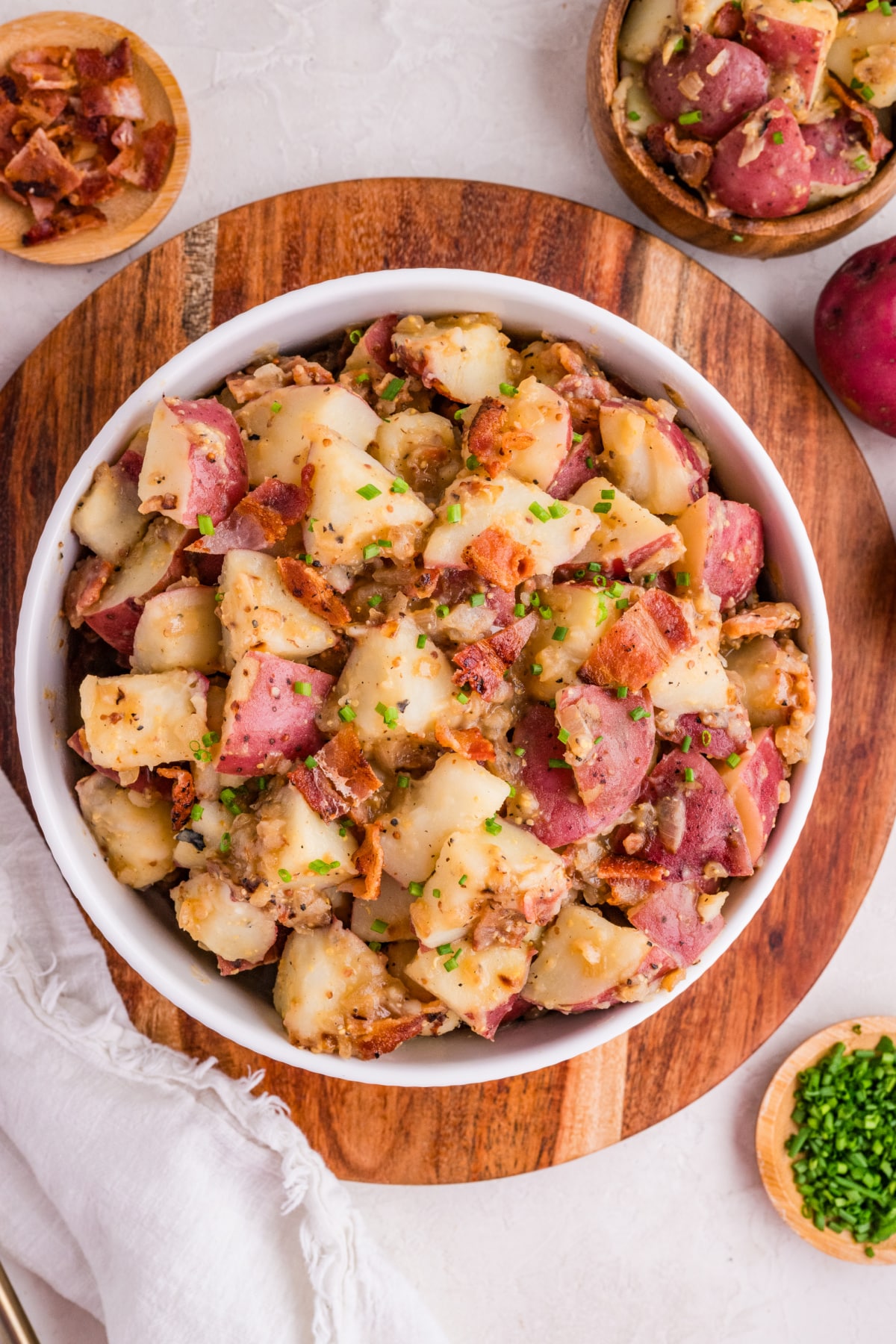 german potato salad with bacon and two mustards German potato salad with bacon, red potatoes, and mustard dressing in a serving bowl with chives