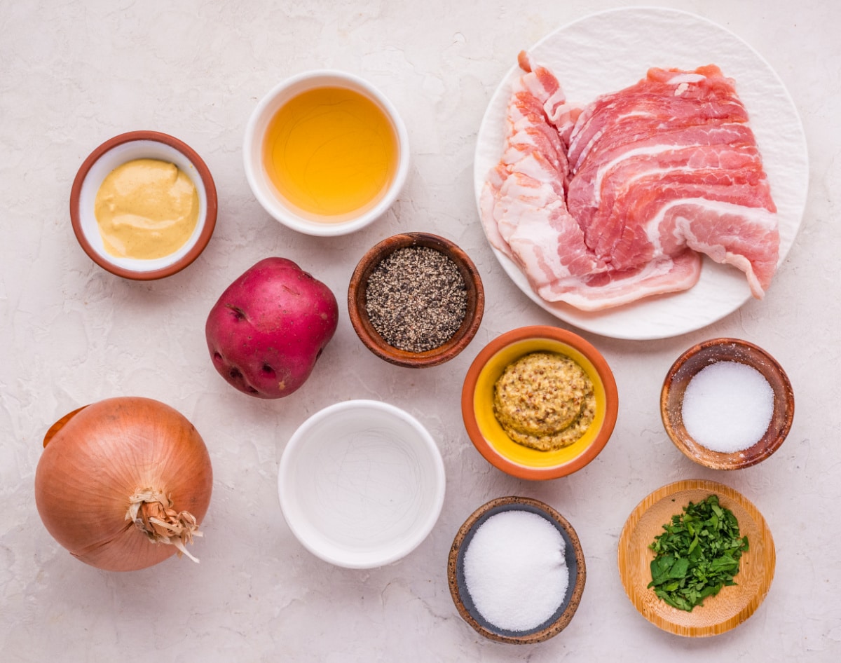 ingredients for german potato salad with bacon and mustard dressing German potato salad ingredients including red potatoes, bacon, onion, apple cider vinegar, Dijon and whole grain mustard, and herbs
