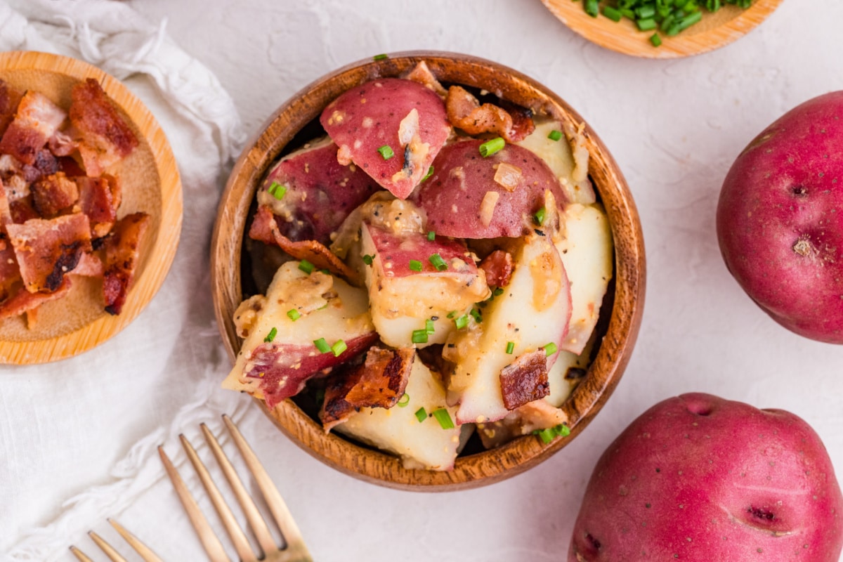 German potato salad with bacon and mustard dressing German potato salad with red potatoes, bacon, and mustard dressing served in a wooden bowl with chives
