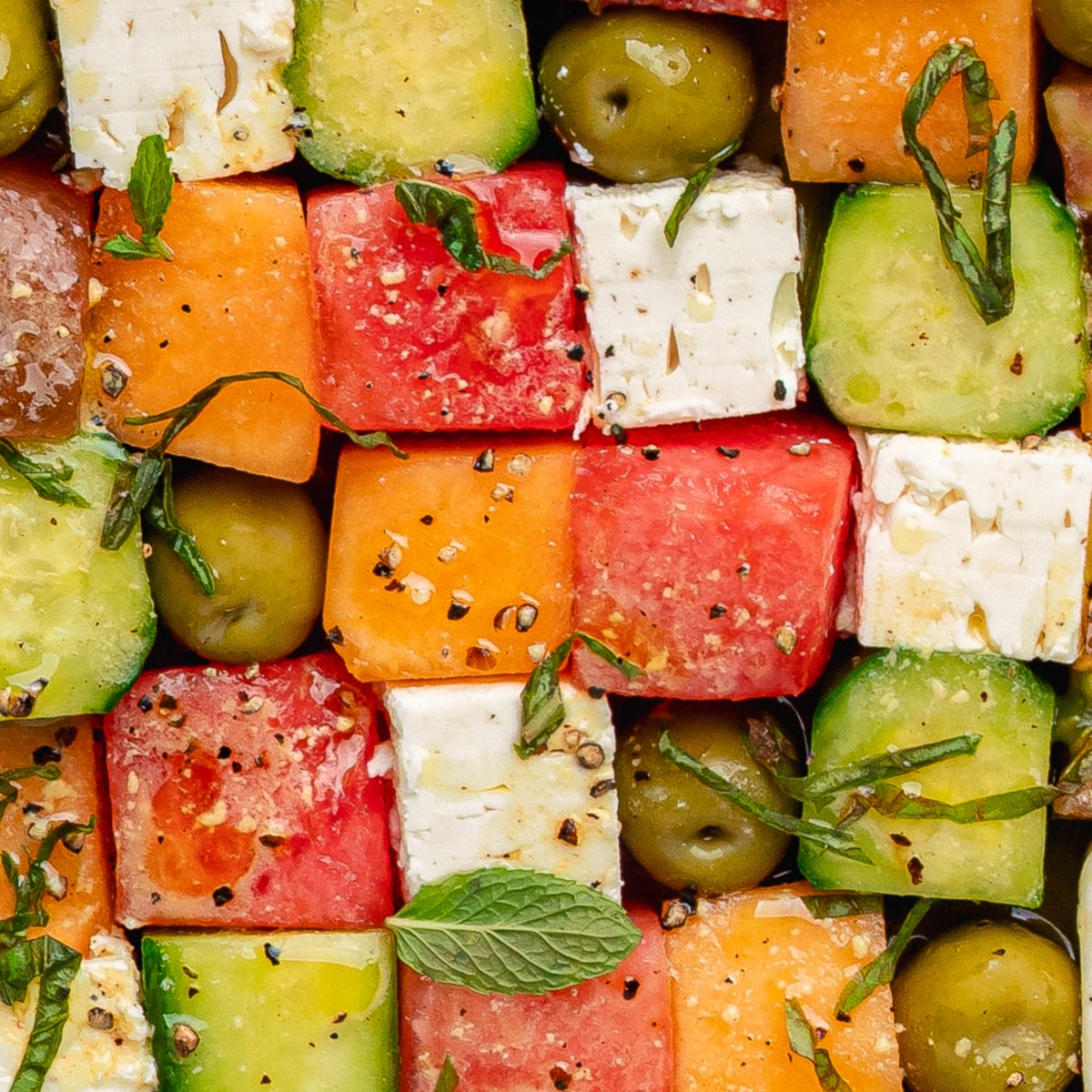 Greek mosaic salad with watermelon, feta, cucumber, olives, and herbs on a platter