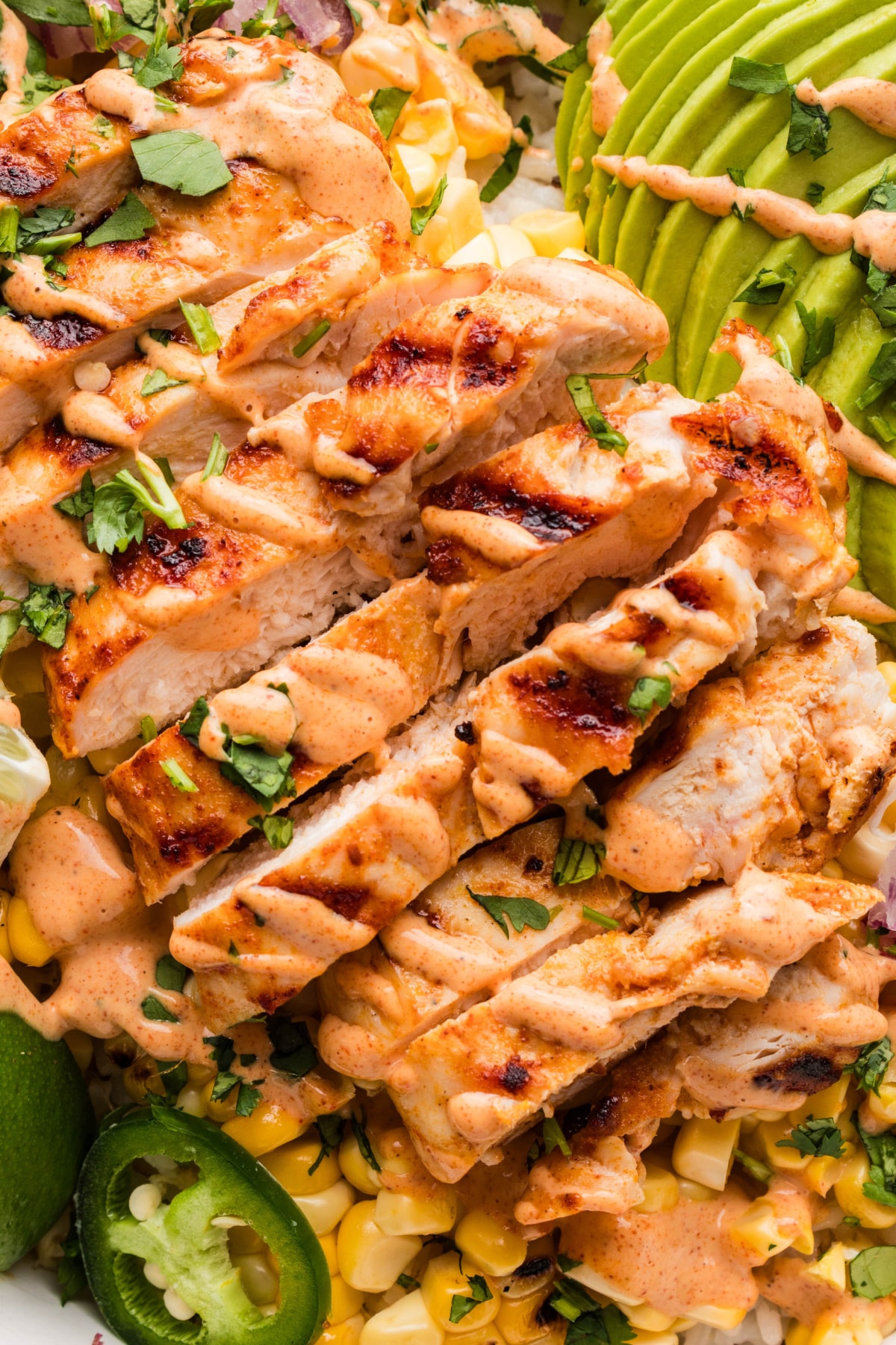 grilled chicken slices with charred corn, jalapeños, avocado, and creamy elote-style sauce over rice