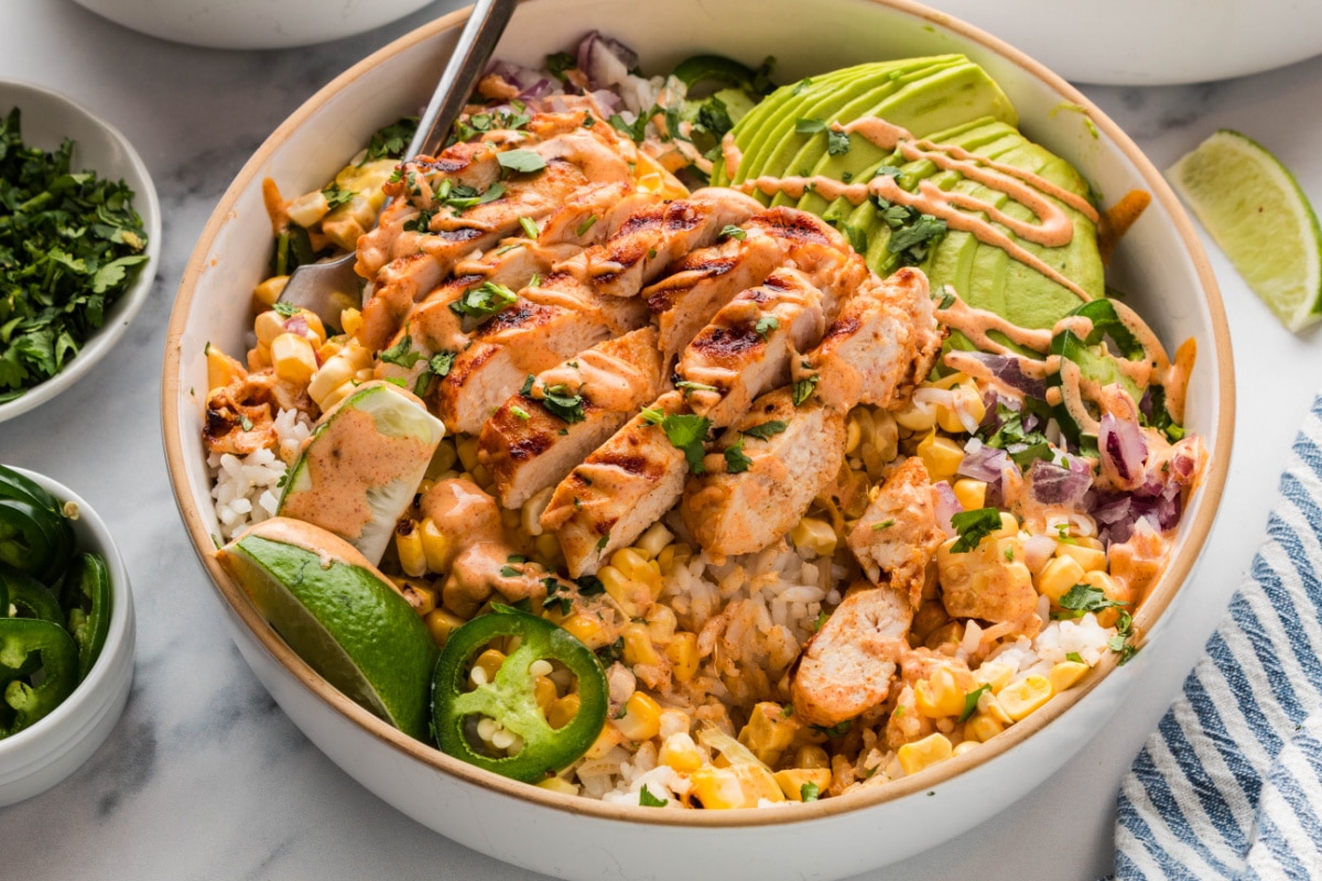 grilled chicken rice bowl with charred corn, avocado slices, jalapeños, red onion, and creamy elote-style sauce