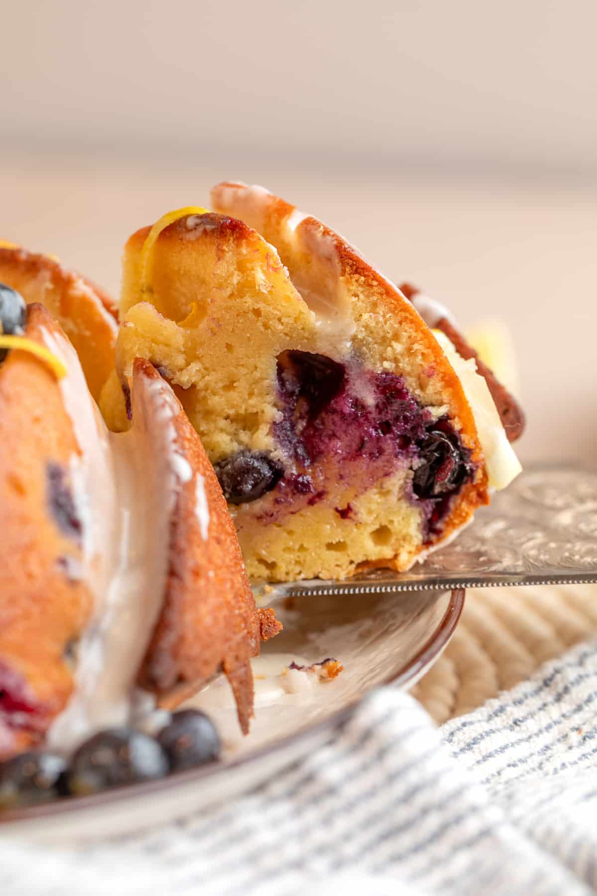 slice of lemon blueberry bundt cake showing interior with baked blueberries and lemon glaze