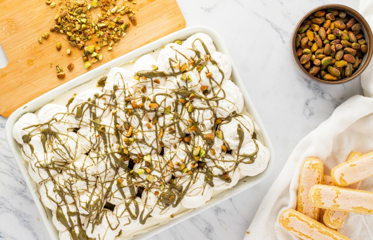 Pistachio Tiramisu in Pan with Whipped Topping and Pistachio Drizzle pistachio tiramisu in a 9x13 pan topped with whipped cream pistachio drizzle and chopped pistachios with ladyfingers and pistachios on the side