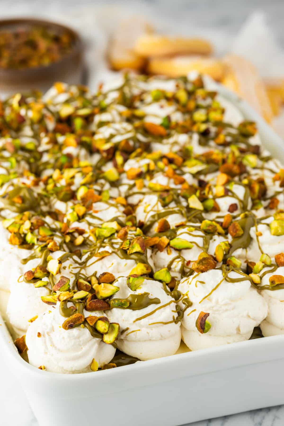 Pistachio Tiramisu with Piped Cream and Pistachio Topping pistachio tiramisu with piped whipped cream topping finished with pistachio drizzle and chopped pistachios