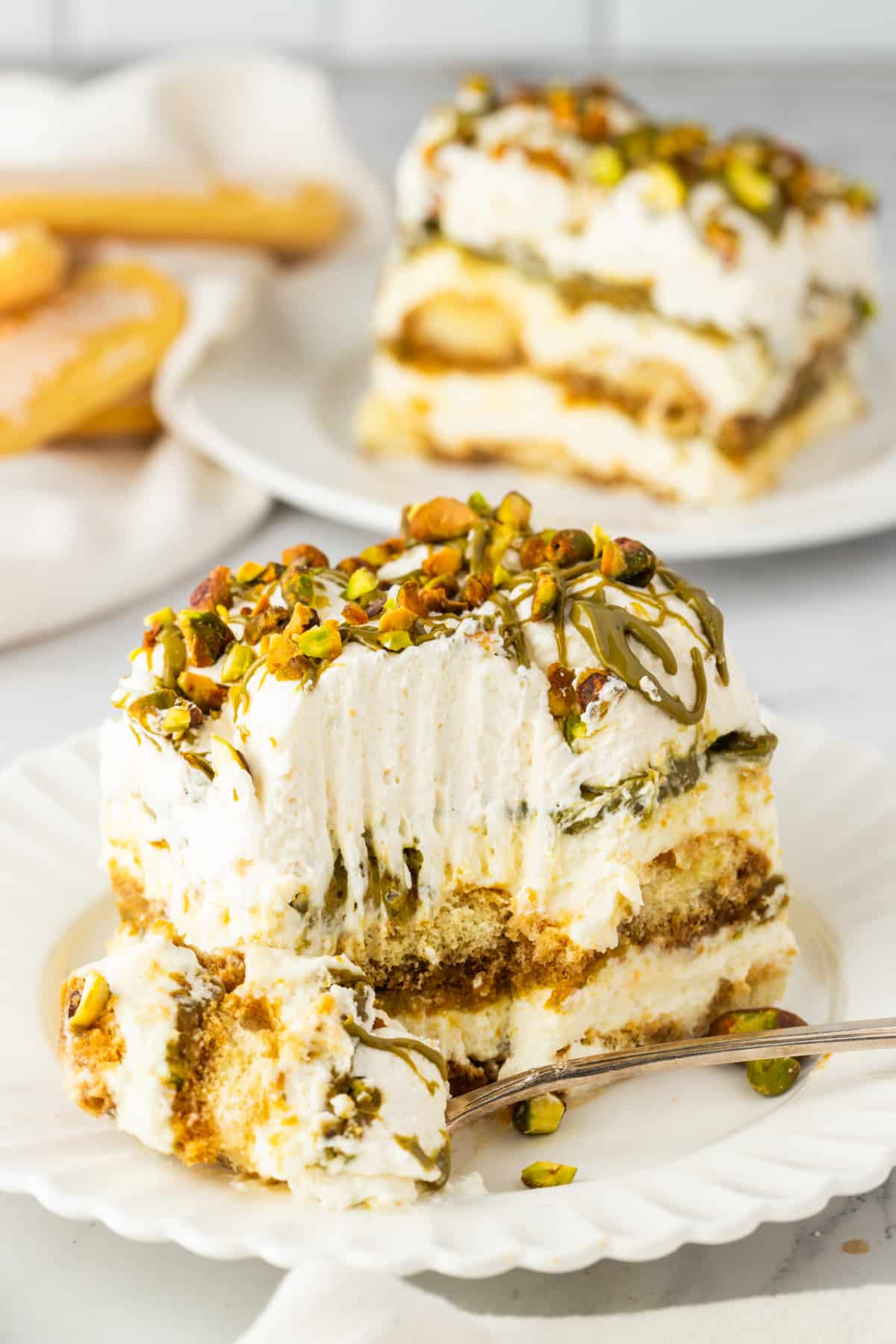 Tiramisu Slice with Bite Showing Creamy Layers slice of tiramisu with a bite taken showing mascarpone layers espresso soaked ladyfingers and pistachio cream with chopped pistachios
