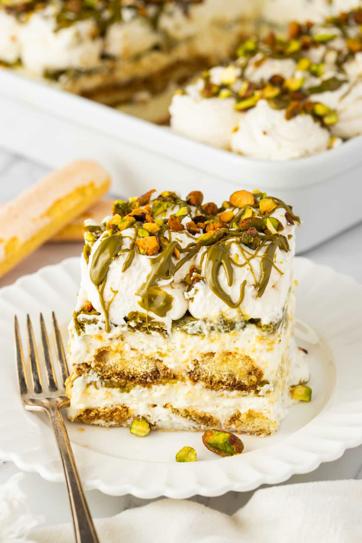 Pistachio Tiramisu Slice with Creamy Layers and Pistachio Drizzle pistachio tiramisu slice with layers of mascarpone cream and espresso soaked ladyfingers topped with pistachio cream and chopped pistachios