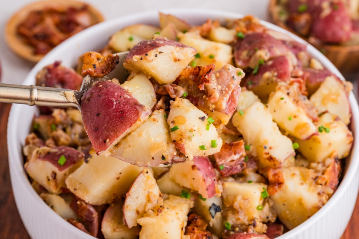 serving warm potato salad with bacon and mustard dressing warm potato salad with bacon, red potatoes, and mustard dressing being served with a fork