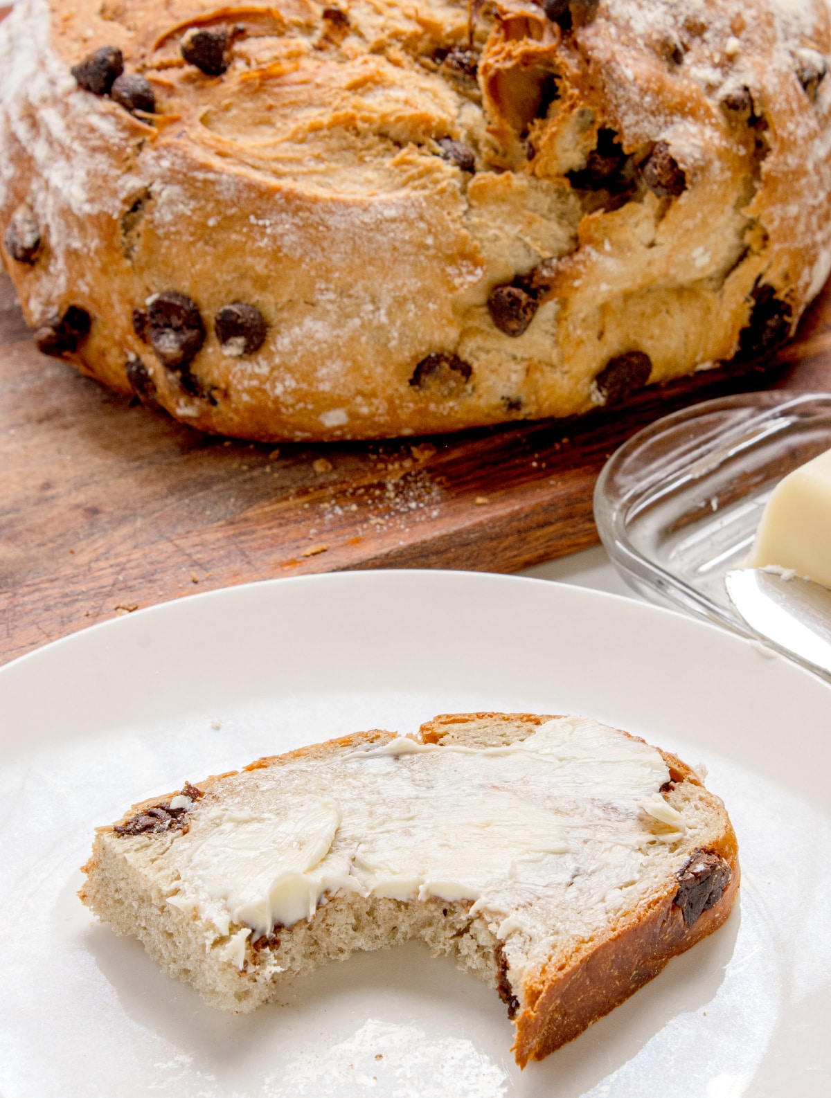 slice of chocolate chip bread with butter and a bite taken on a white plate