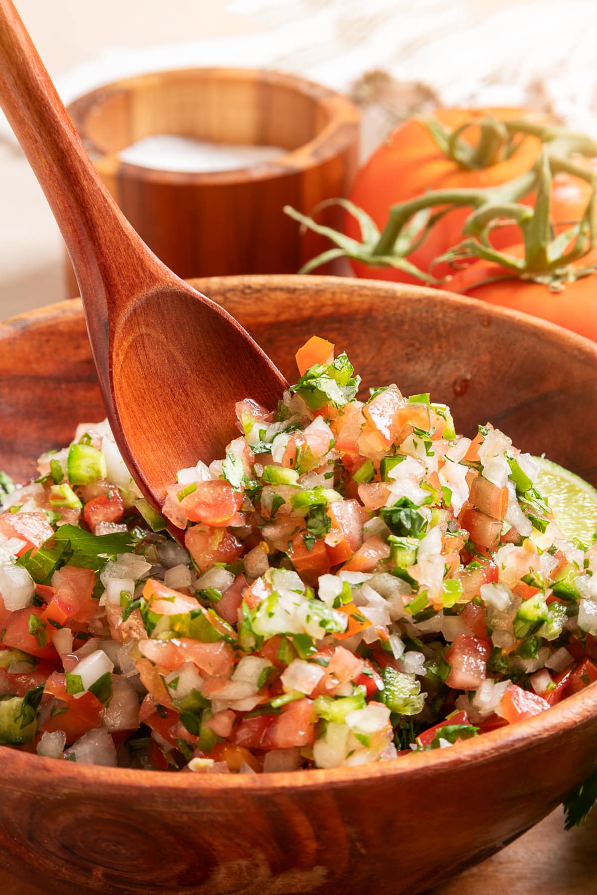 Serving spoon scooping chunky pico de gallo with tomatoes, onion, jalapeño, cilantro, and lime
