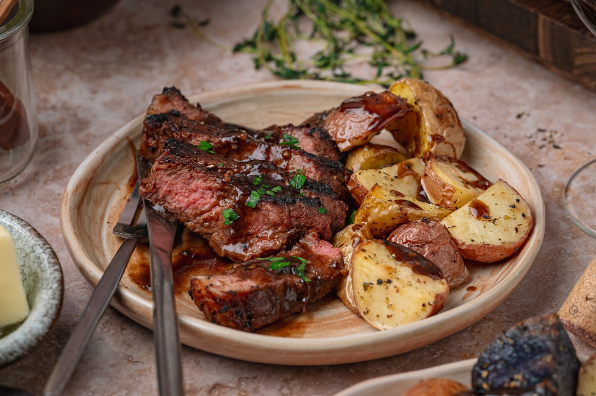 Medium rare sliced steak with dark pan sauce and roasted potatoes. Cocoa crusted steak with stout pan sauce served with roasted potatoes on a ceramic plate.