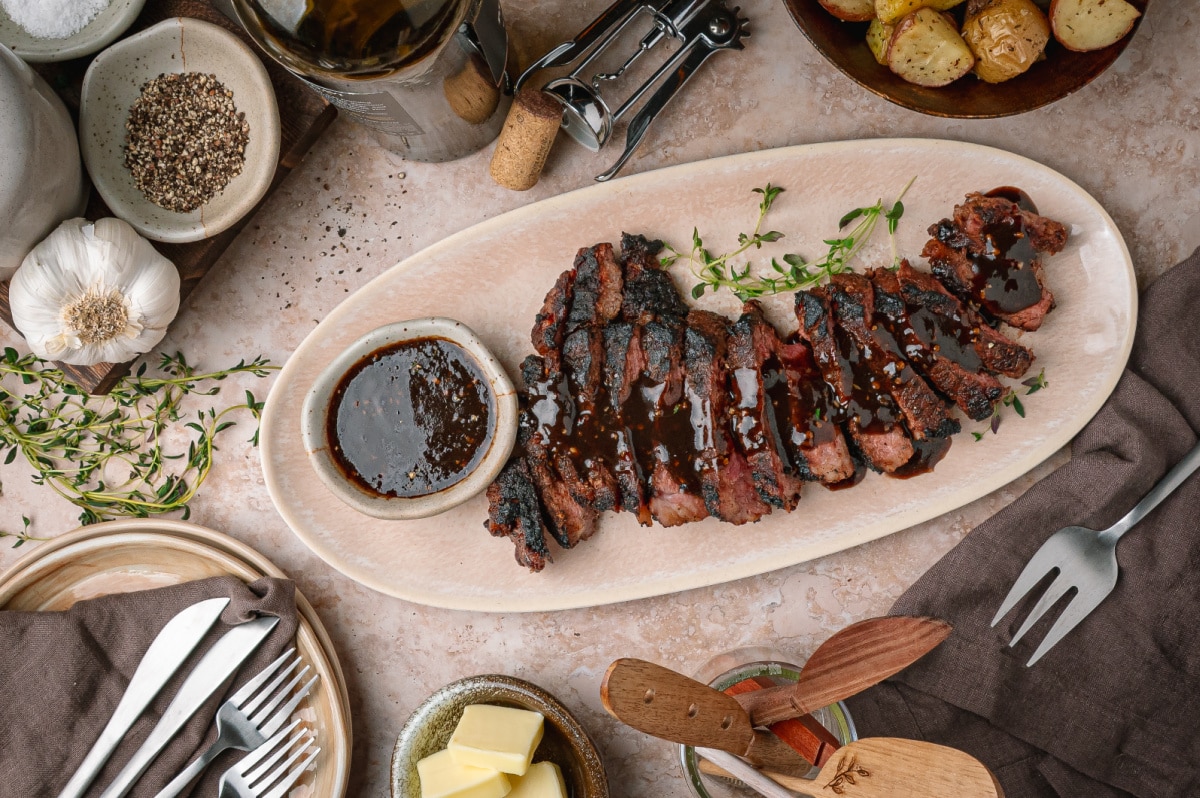 Sliced cocoa rubbed steak served with dark stout pan sauce. Cocoa rubbed steak with dark stout pan sauce sliced on a serving platter with extra sauce on the side.