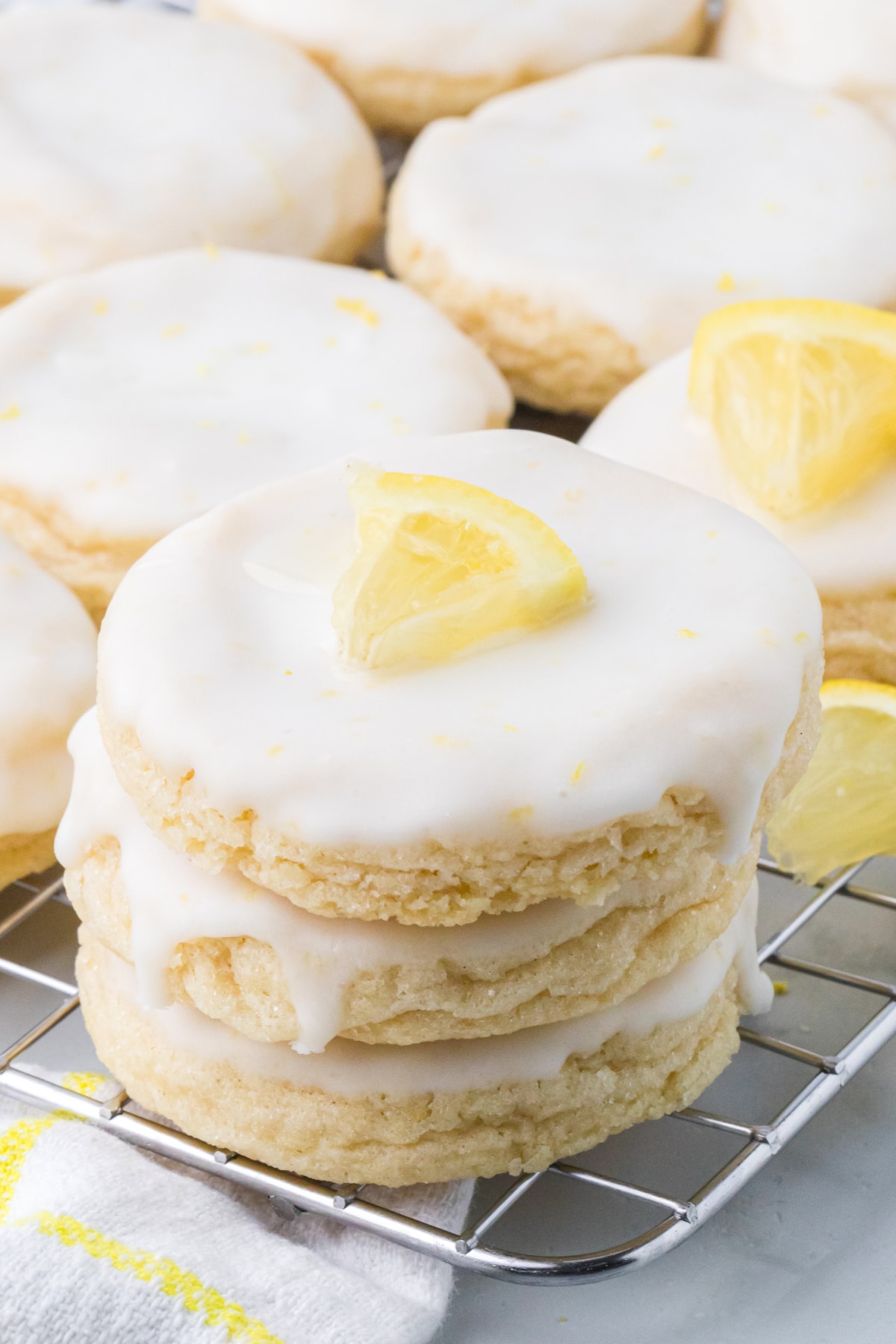 Glazed lemon sugar cookies stacked on a cooling rack with thick lemon glaze