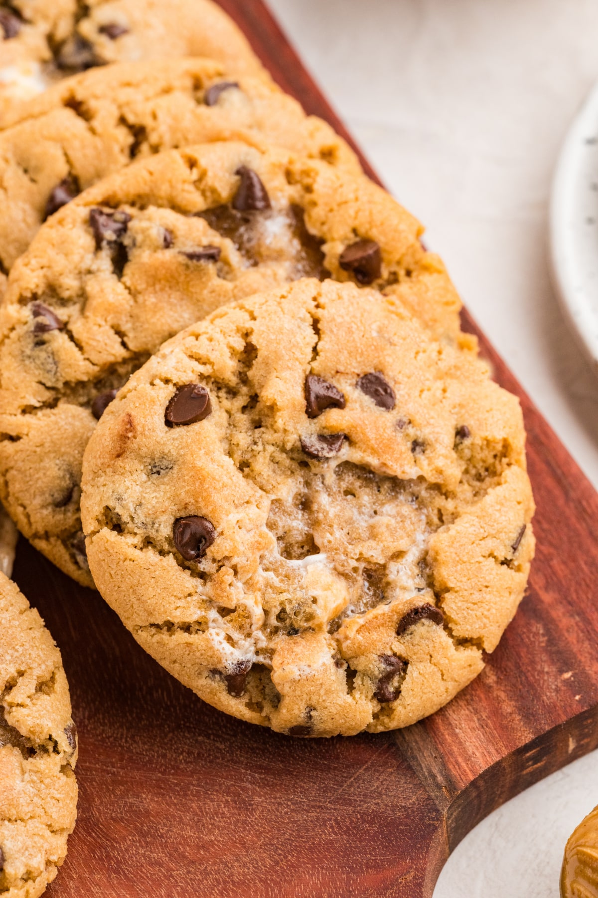 Thick peanut butter cookie with toasted marshmallow pockets and mini chocolate chips on a wooden serving board.